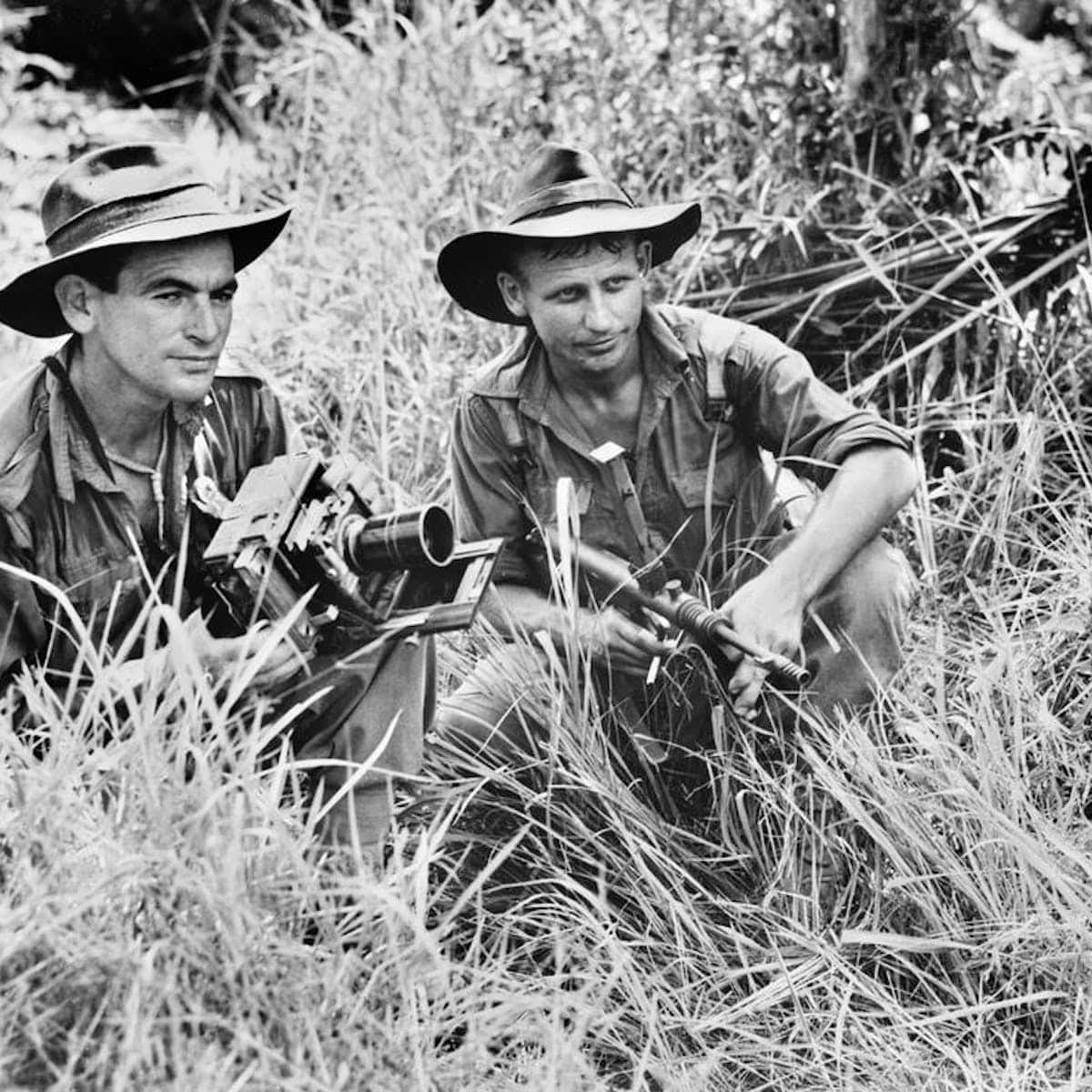 Ww2 桌布 壁紙 — 兩名戴寬邊帽的士兵蹲在高草叢中，在茂密的叢林環境中手持步槍。