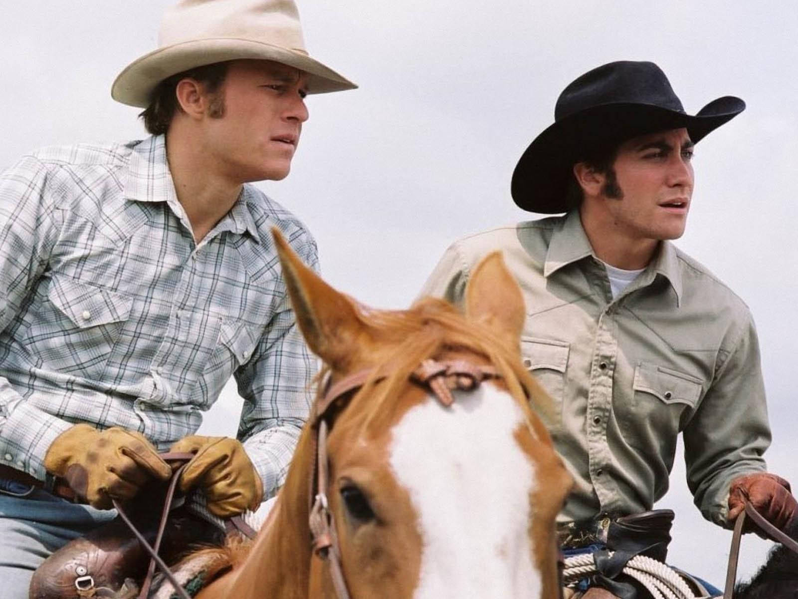 brokeback mountain 桌布 壁紙 — 兩名戴帽子的牛仔並排騎馬，背景是陰天，前景特寫一匹棕白相間的馬頭。