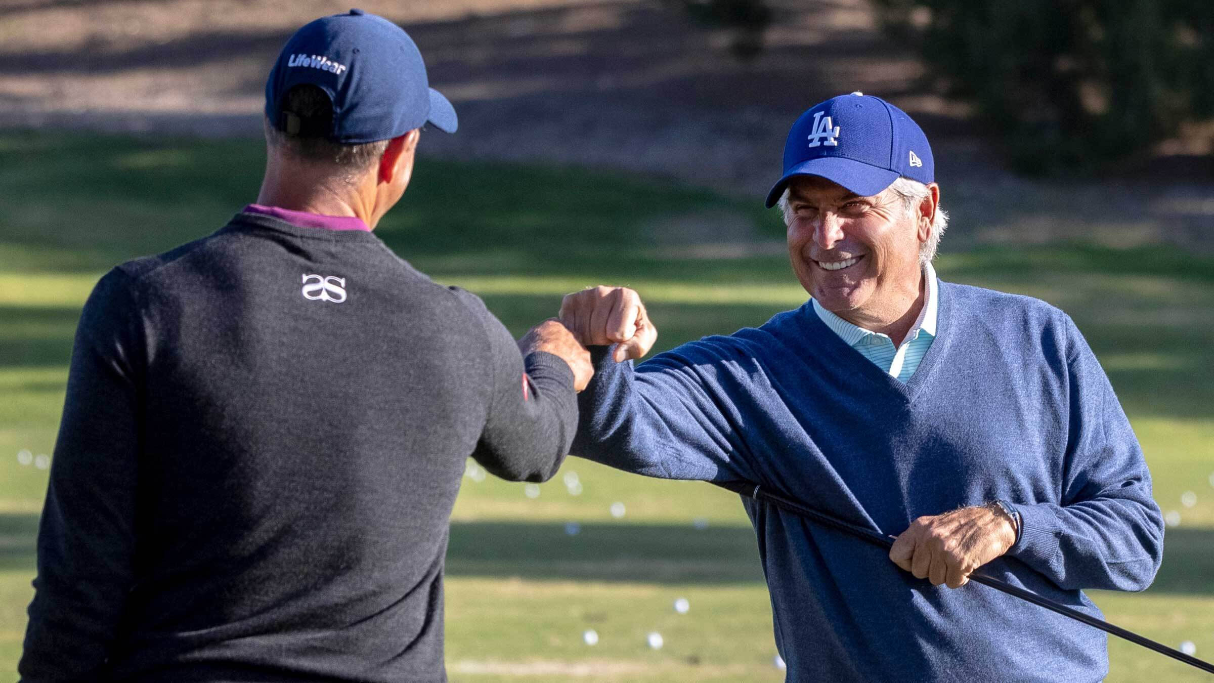 adam scott 桌布 壁紙 — 兩名戴帽微笑的男子在陽光明媚的高爾夫球場上，在散落的球和綠草間互相碰拳。