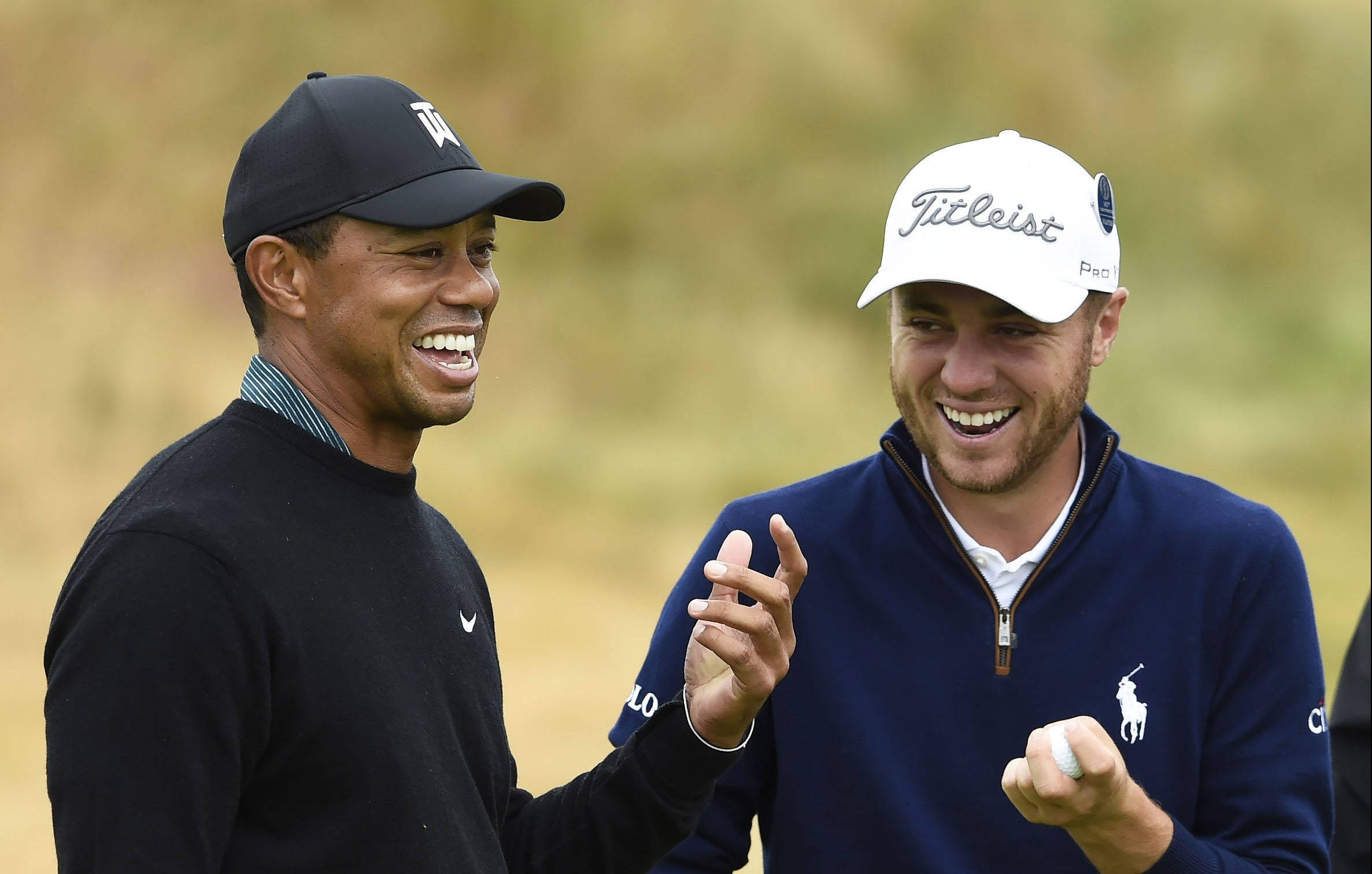 高爾夫 桌布 壁紙 — 兩名戴帽微笑的高爾夫球手在陽光明媚的球場上分享歡樂時刻，背景是模糊的草地。