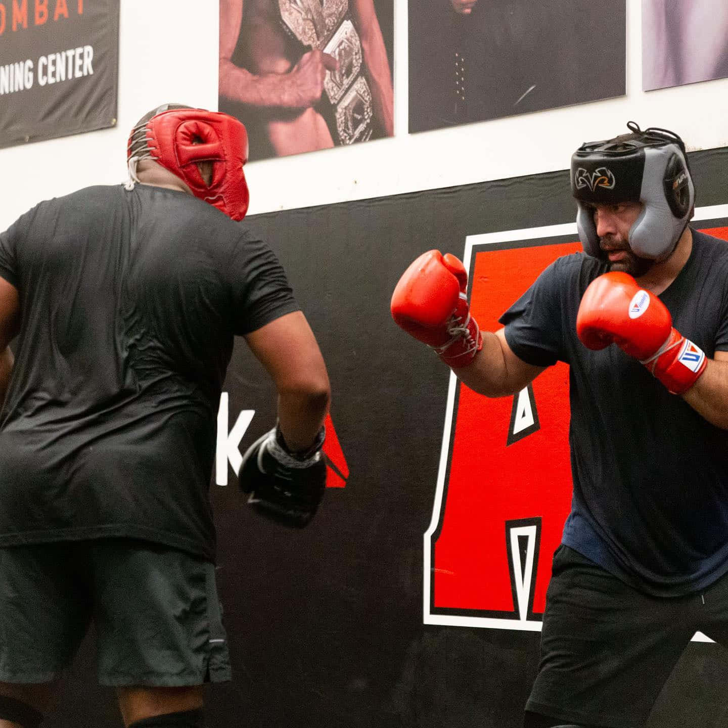 MMA 桌布 壁紙 — 兩名戴紅色手套和頭部護具的拳擊手在牆上貼有冠軍海報的健身房內激烈對打。