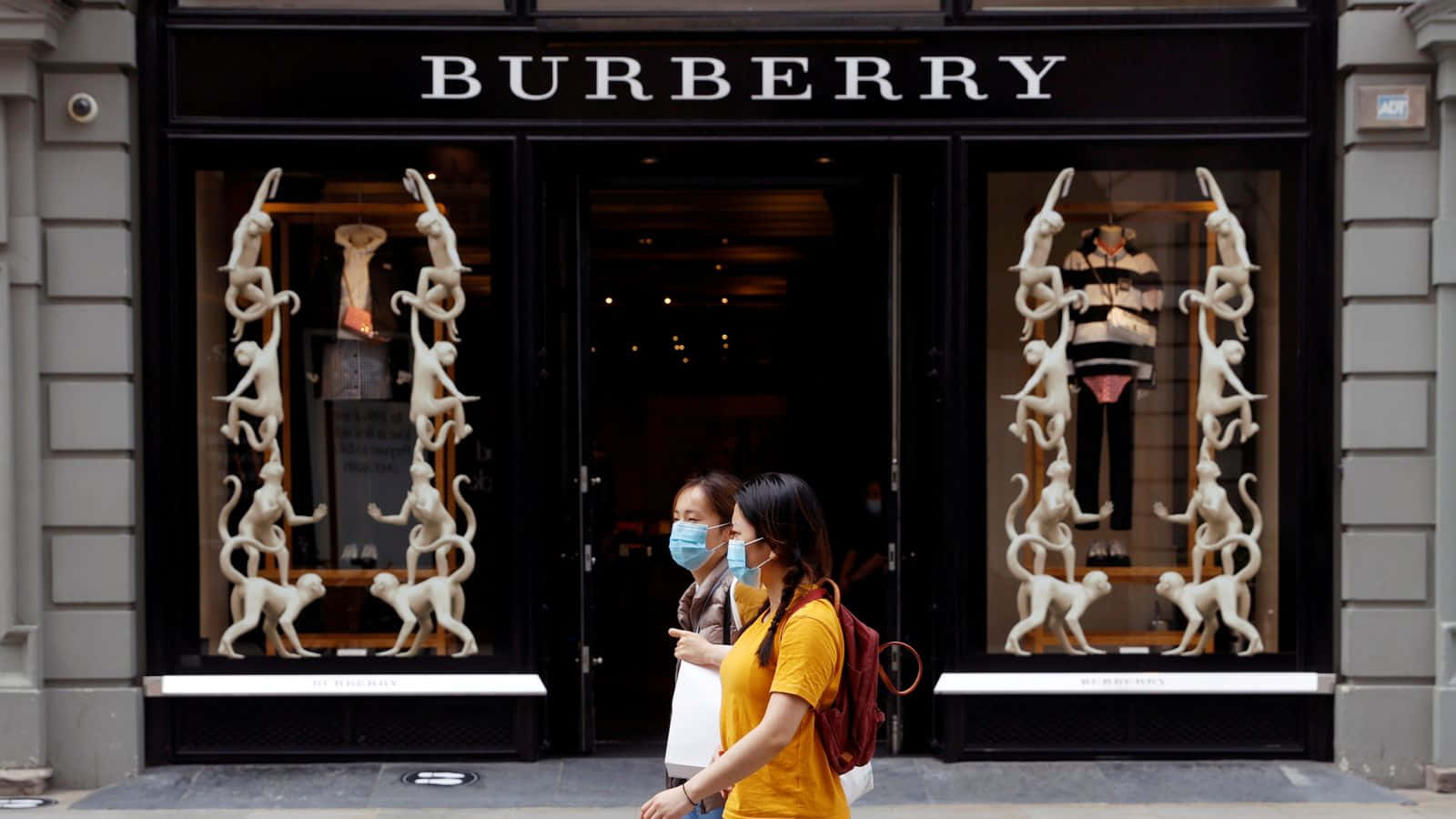 Burberry 桌布 壁紙 — 兩名戴著口罩的行人經過一間Burberry商店，其櫥窗內有引人注目的白色猴子雕塑。