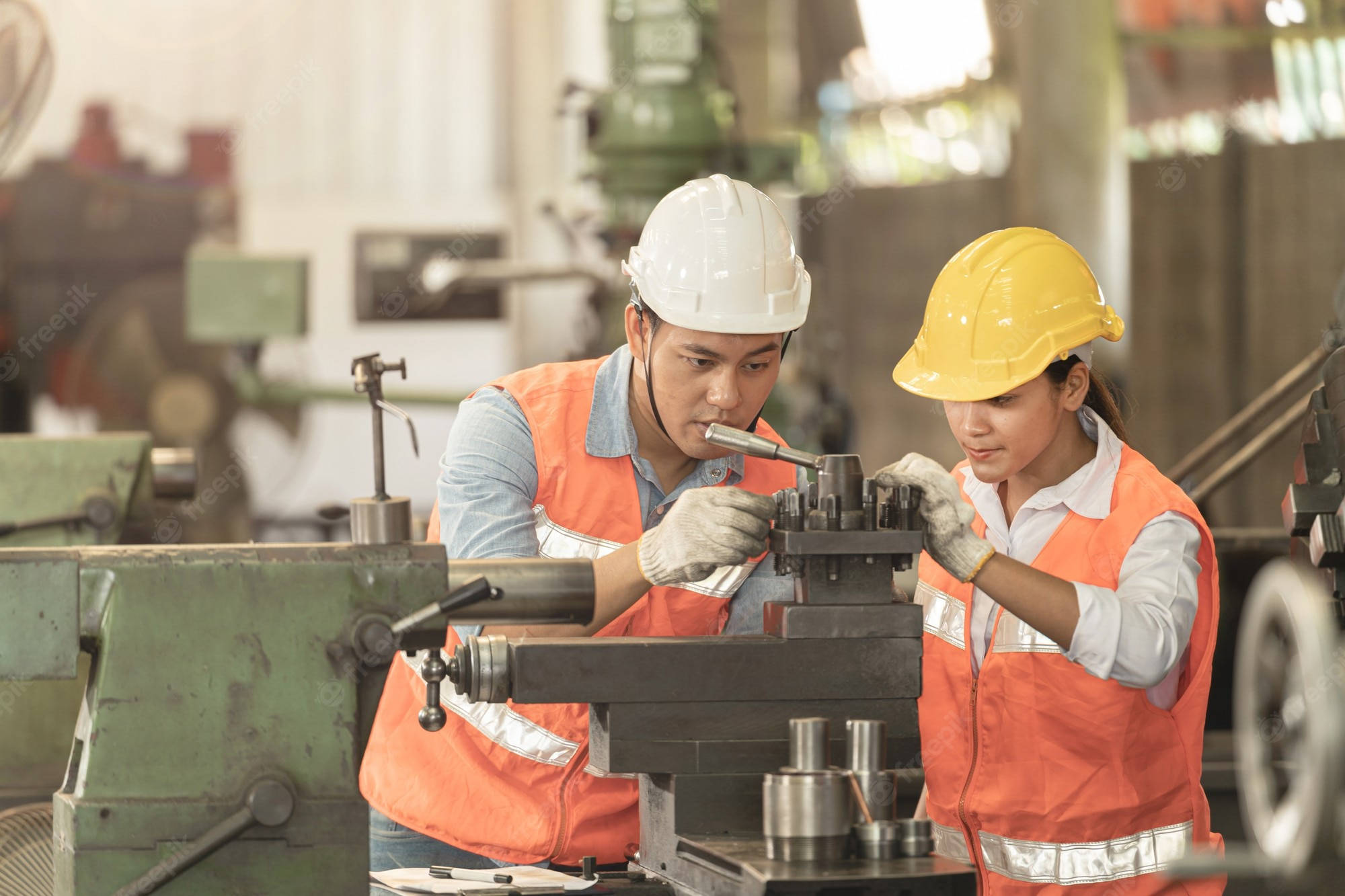 machines 桌布 壁紙 — 兩名戴著安全帽和橙色背心的工廠工人在繁忙的工業車間中緊密合作操作金屬加工機器。