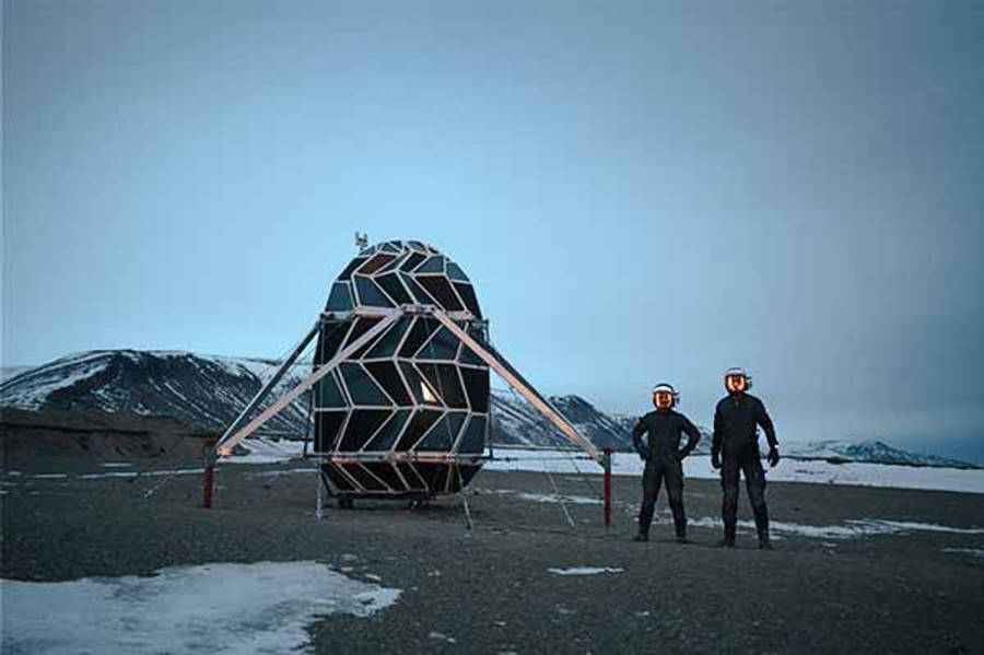 Greenland 桌布 壁紙 — 兩名戴著發光頭盔的太空人站在蒼白天空下，雪地外星景觀中的幾何太空棲息地前。