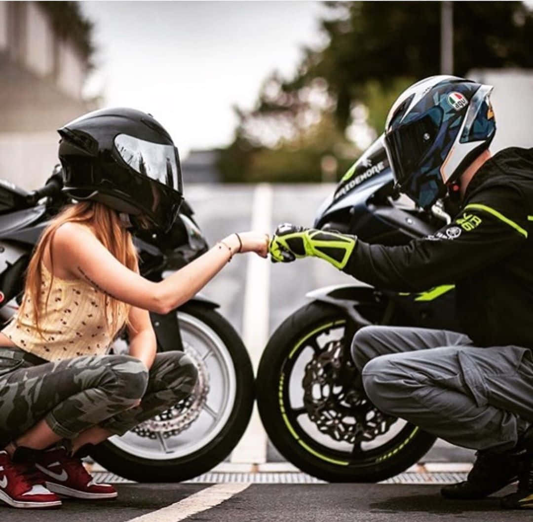 biker 桌布 壁紙 — 兩名戴著頭盔的摩托車手在鋪砌的道路上蹲在他們的摩托車旁互相碰拳。