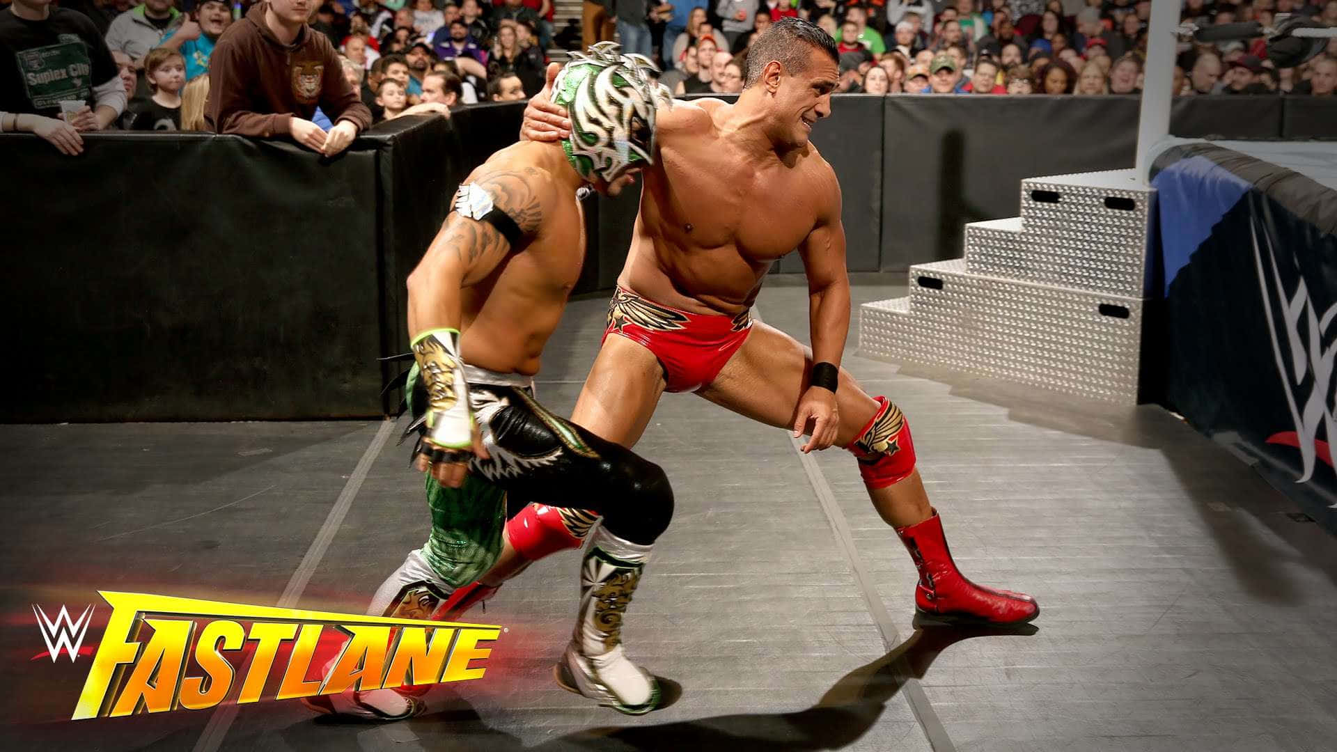 WWE 桌布 壁紙 — 兩名戴面具的摔角手在燈光明亮的擂台上激烈糾纏，背景是歡呼的人群。