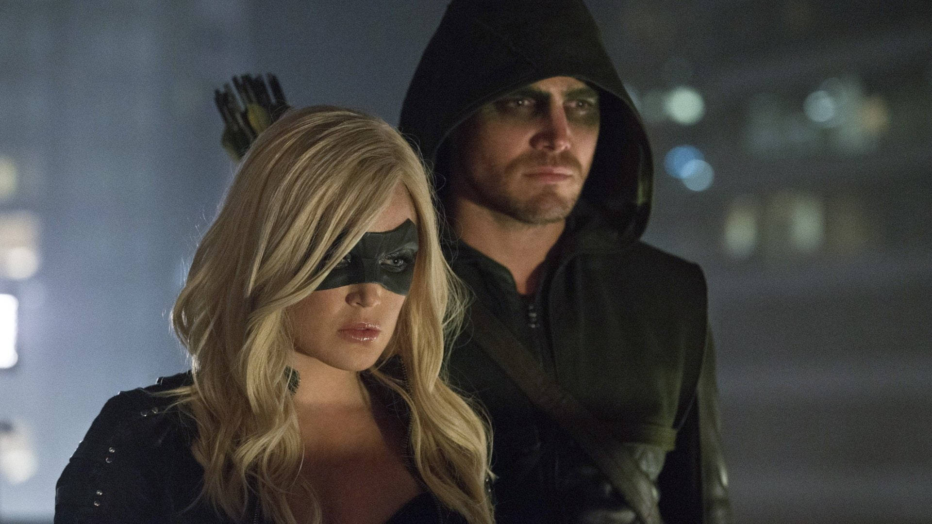 Black Canary 桌布 壁紙 — 兩名戴面具的義警在夜晚的城市景觀中並肩而立，一人金髮，另一人穿著連帽外套，背上背著箭。
