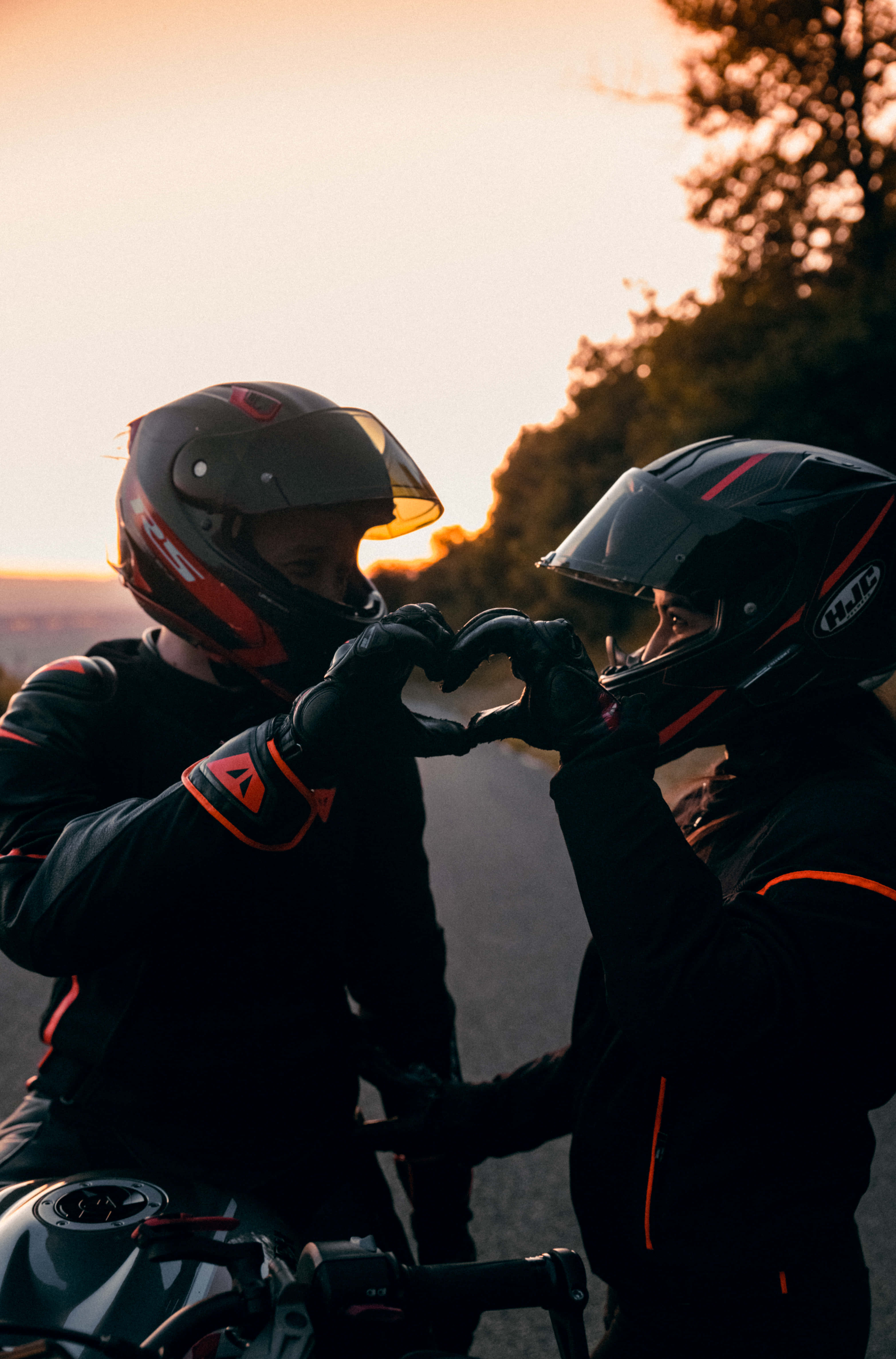 biker 桌布 壁紙 — 兩名戴頭盔的摩托車手戴著手套的手在溫暖的日落天空下形成心形。