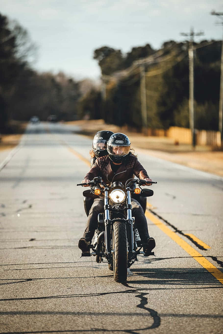 biker 桌布 壁紙 — 兩名戴頭盔的騎士在陽光明媚的鄉村道路上，騎著一輛帶有鍍鉻裝飾和發光頭燈的經典摩托車巡航。