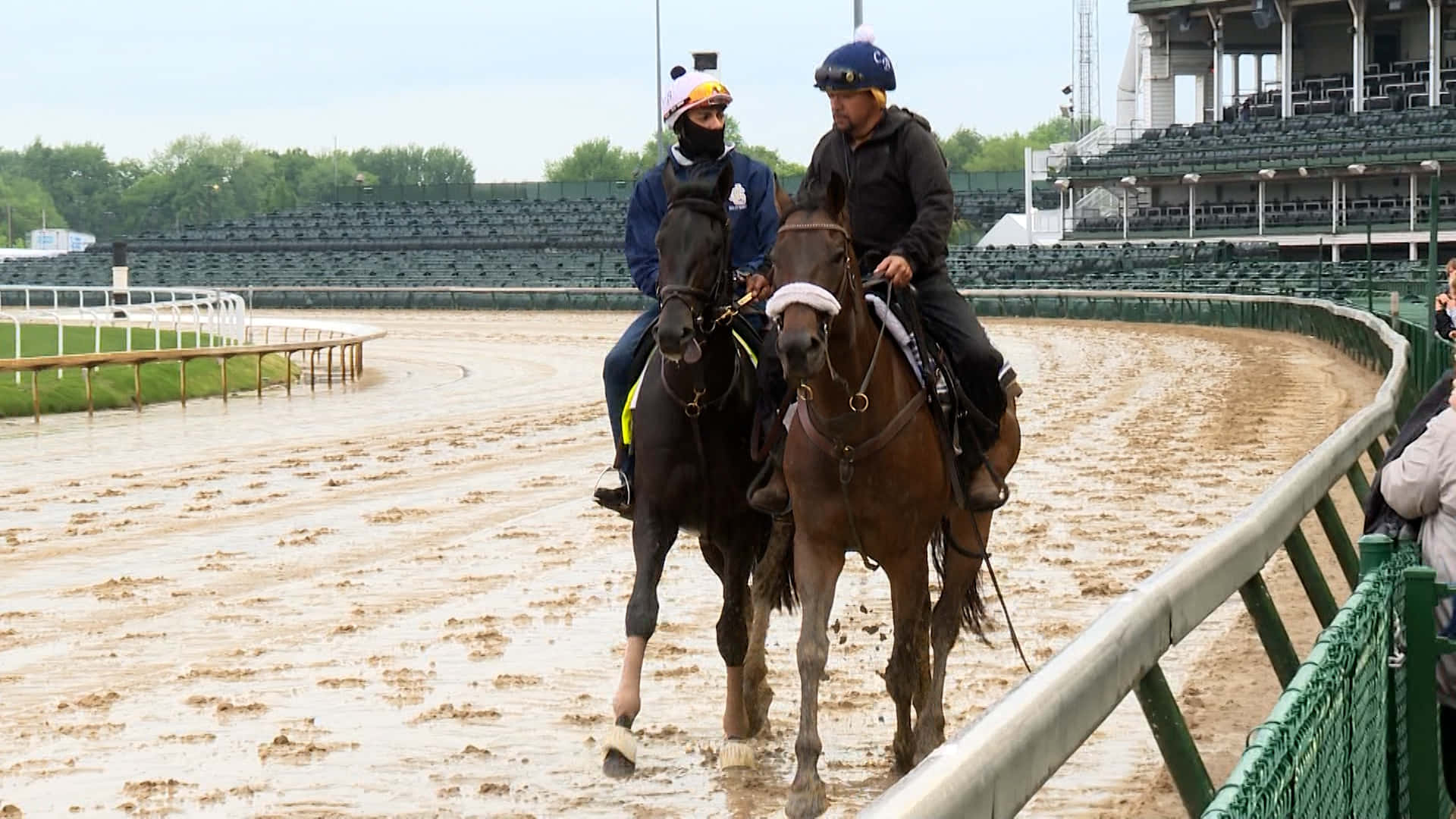 Kentucky Derby 桌布 壁紙 — 兩名戴頭盔的騎師在陰天帶領他們的馬匹穿過泥濘的賽道。