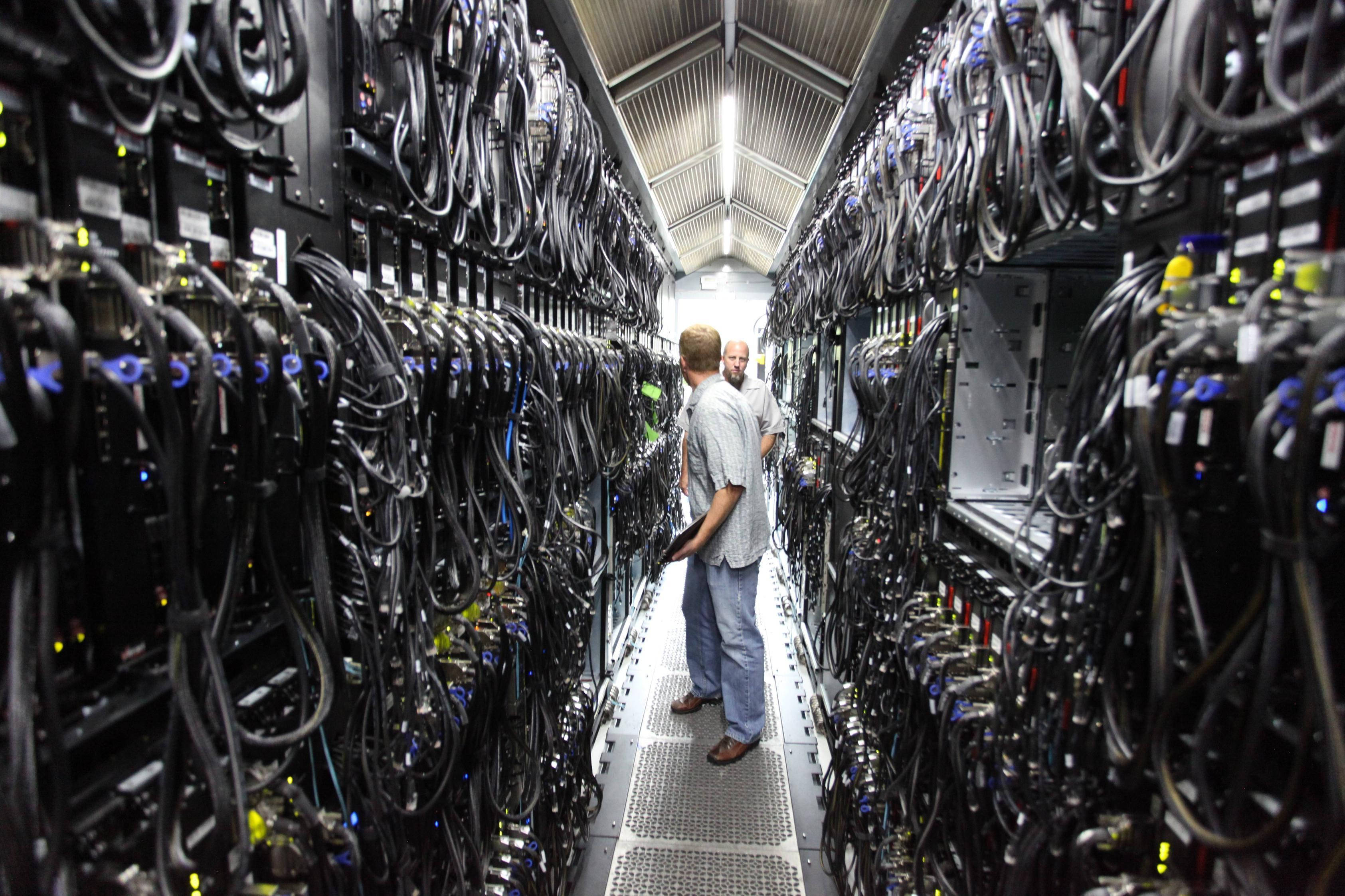 data 桌布 壁紙 — 兩名技術員在光線昏暗的資料中心內，走過高聳伺服器機架之間的狹窄通道。