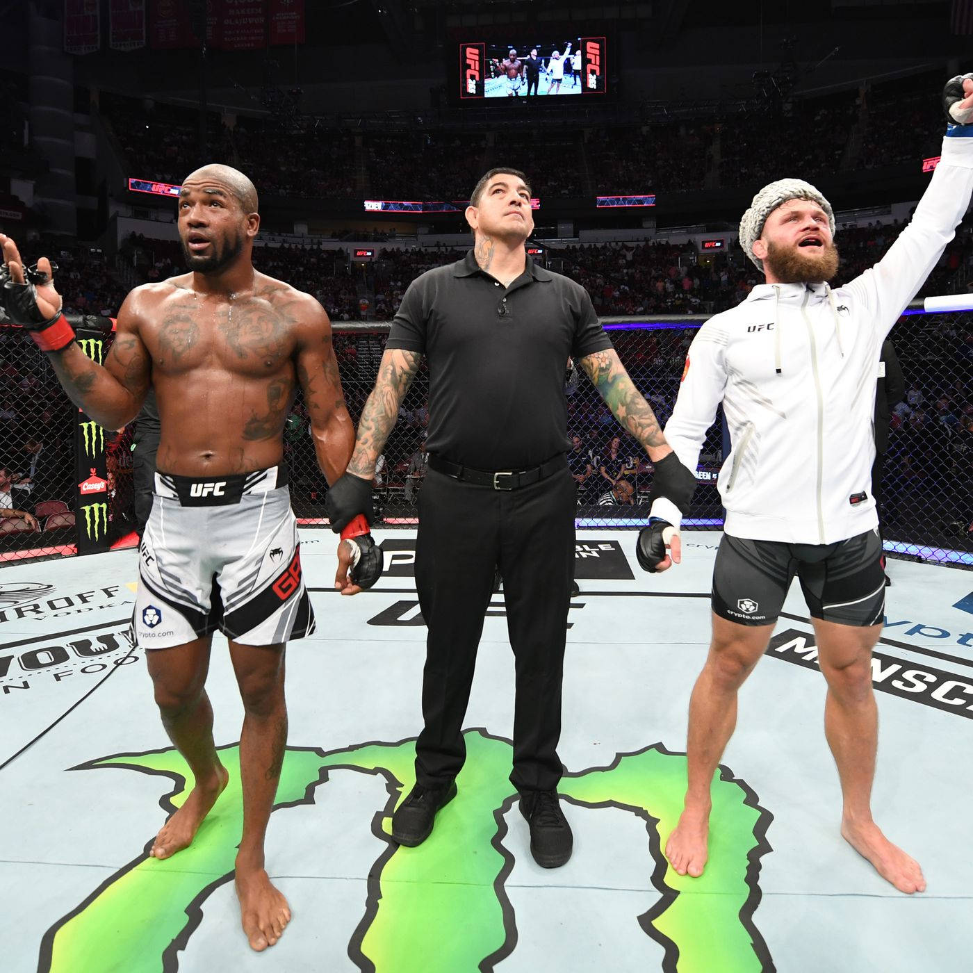 UFC 桌布 壁紙 — 兩名拳手和一名裁判在UFC八角籠內比賽後站立，其中一名拳手舉起手臂慶祝勝利。
