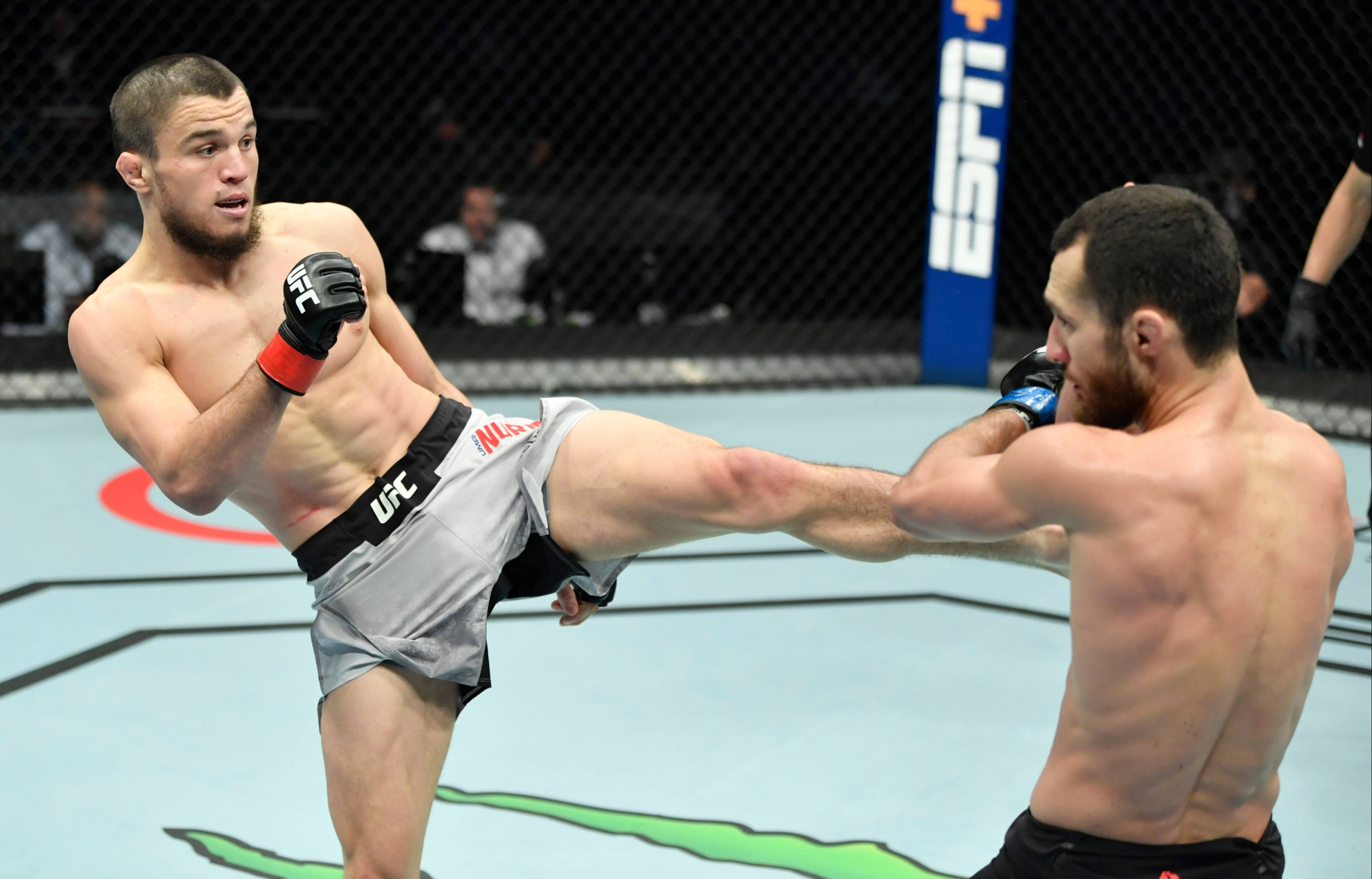MMA 桌布 壁紙 — 兩名拳手在UFC八角籠中交鋒，其中一人在明亮的場館燈光下向對手頭部踢出一記高踢。