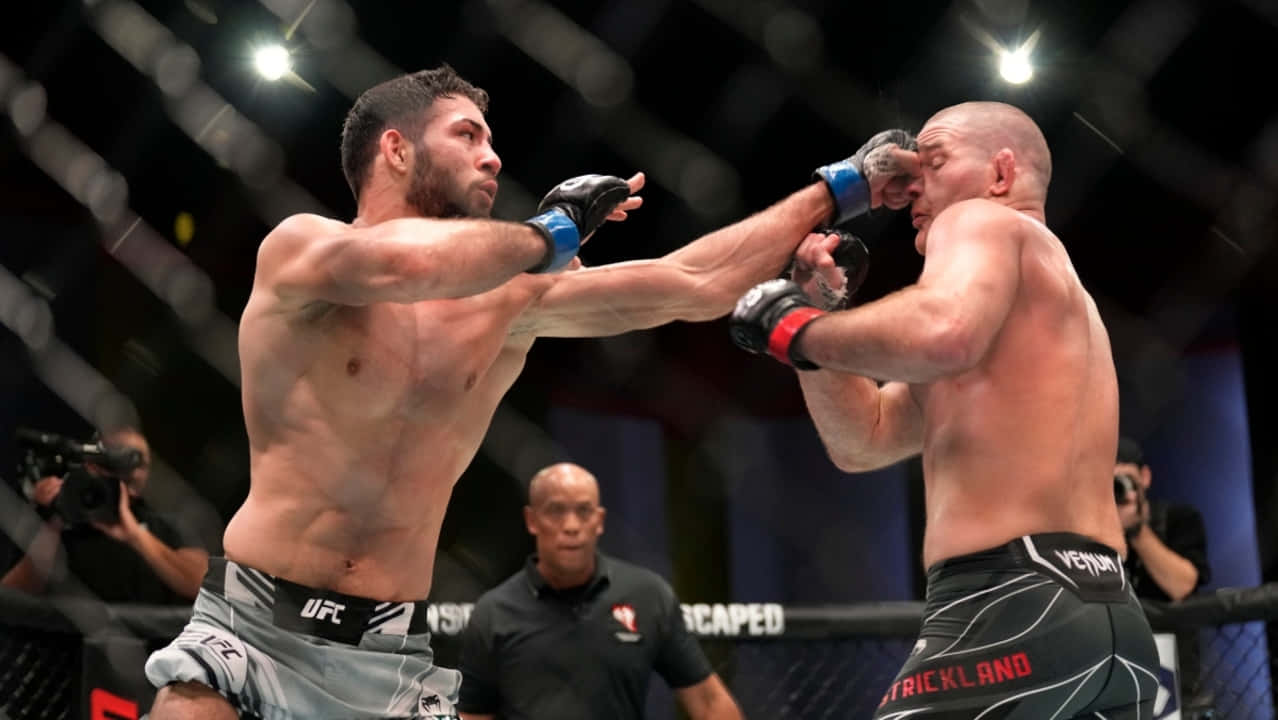 UFC 桌布 壁紙 — 兩名拳手在UFC八角籠中交鋒，其中一人打出強力一拳，裁判在旁密切注視。