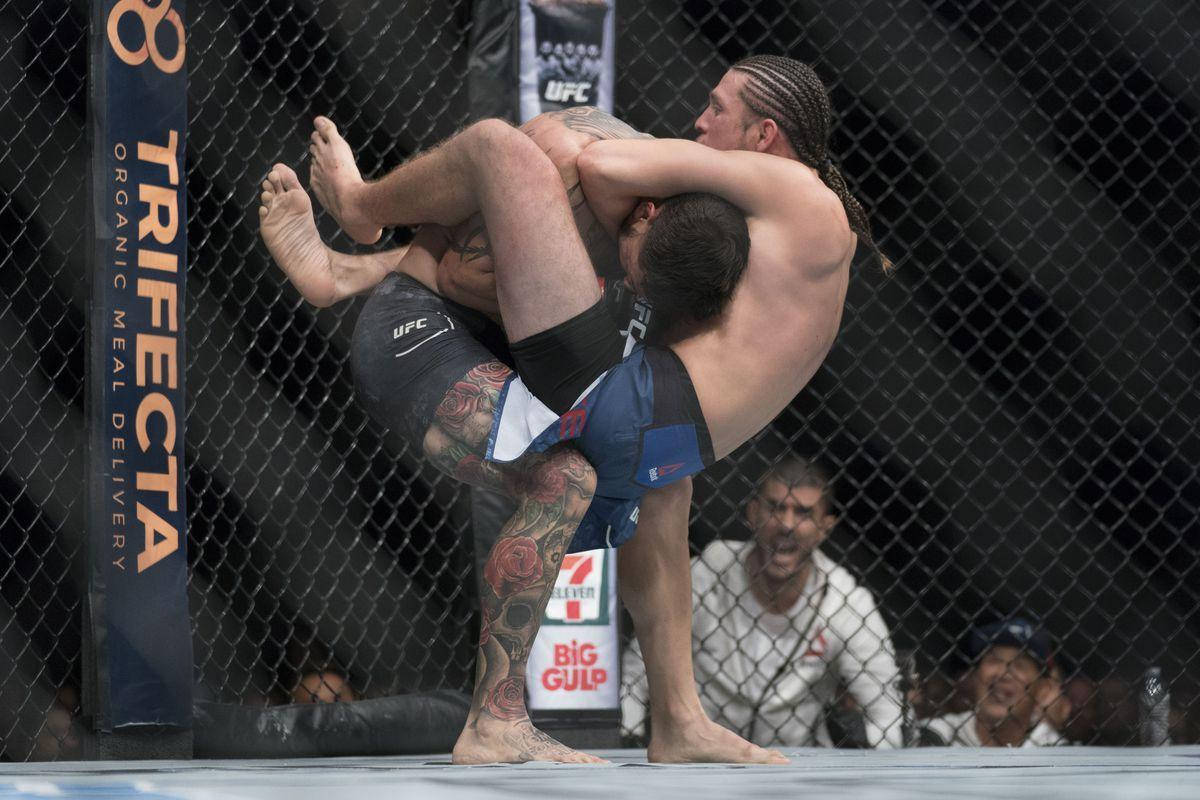 Brian Ortega 桌布 壁紙 — 兩名拳手在UFC八角籠中激烈纏鬥，紋身和辮子在明亮的場館燈光下清晰可見。