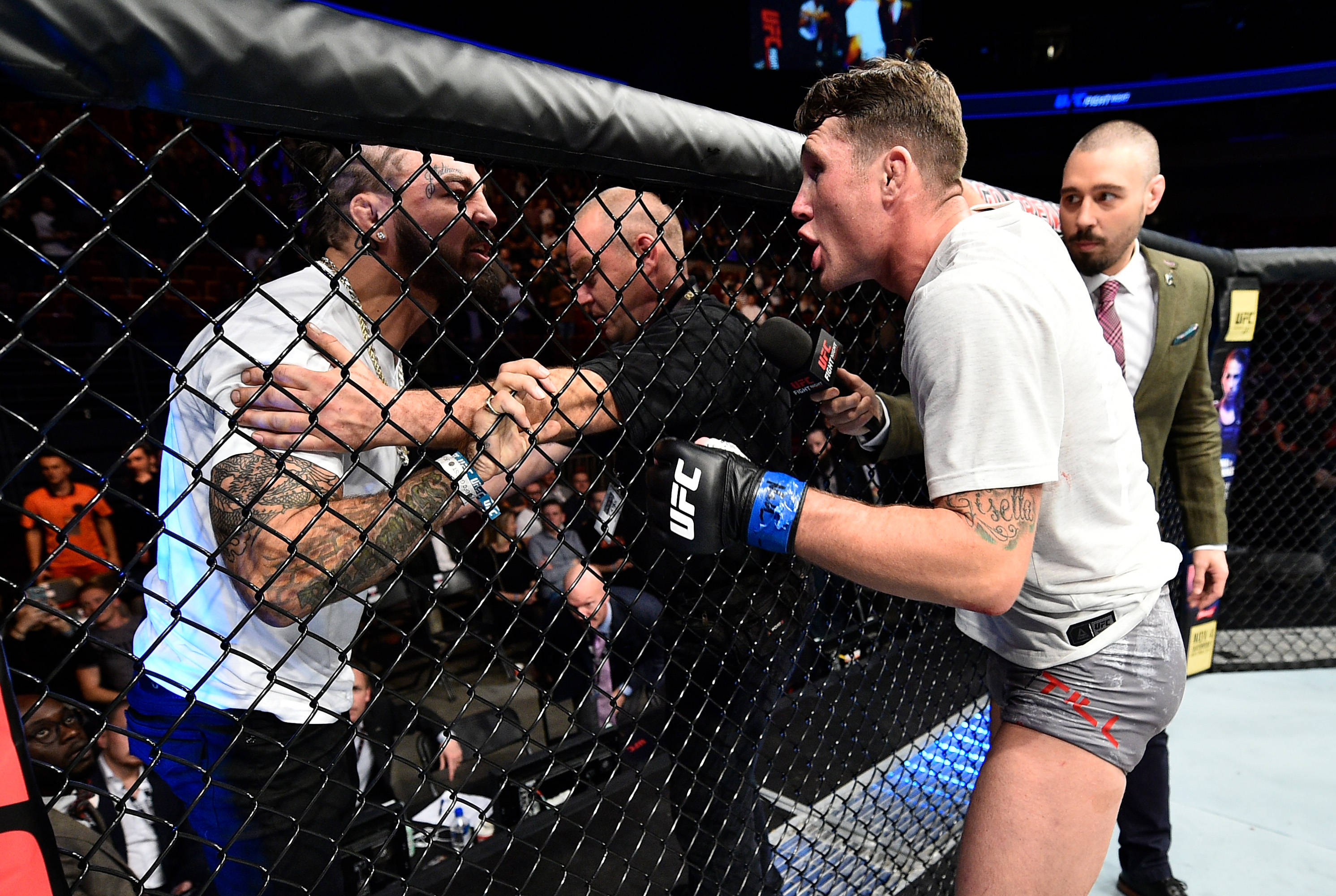 UFC 桌布 壁紙 — 兩名拳手在UFC八角籠內隔著籠網碰撞，裁判在觀眾人群中介入。
