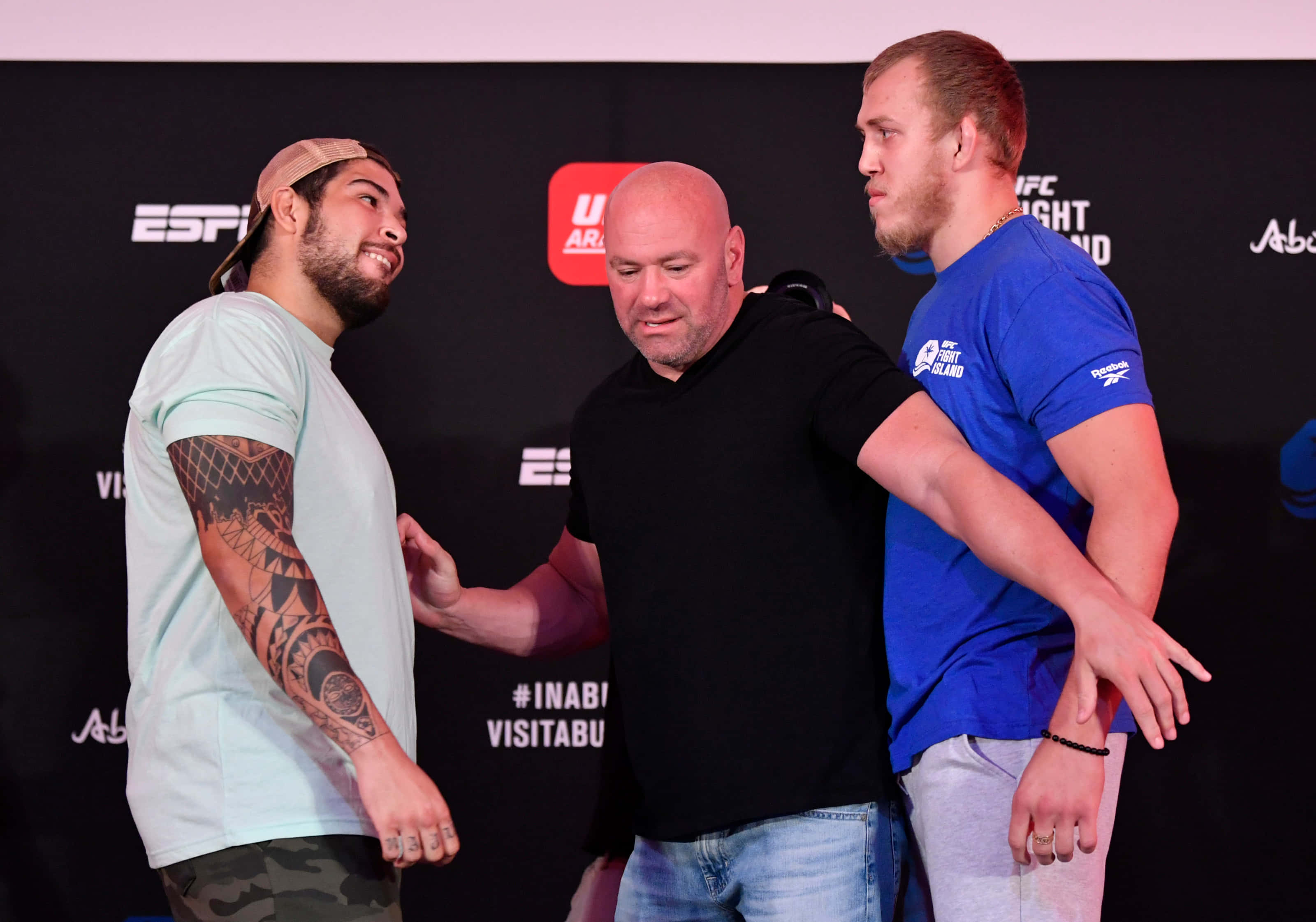UFC 桌布 壁紙 — 兩名拳手在UFC稱重中對峙，Dana White站在他們之間，背景為品牌標誌。