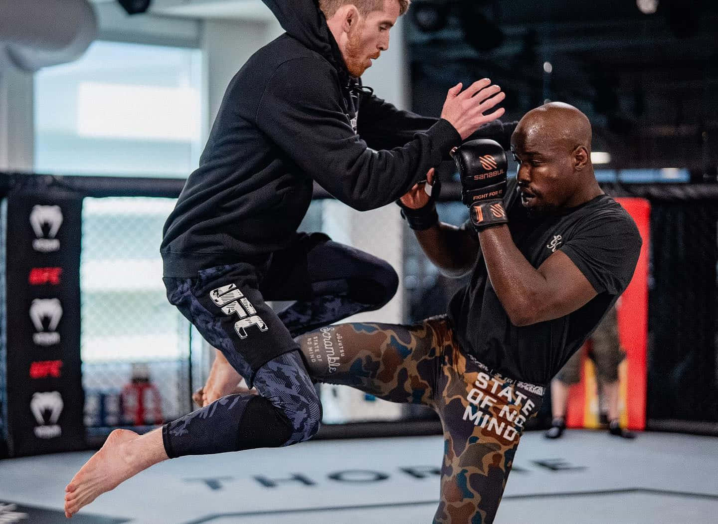 MMA 桌布 壁紙 — 兩名拳手在八角籠中激烈訓練，一人躍起使出高踢，另一人則專注且堅毅地格擋。