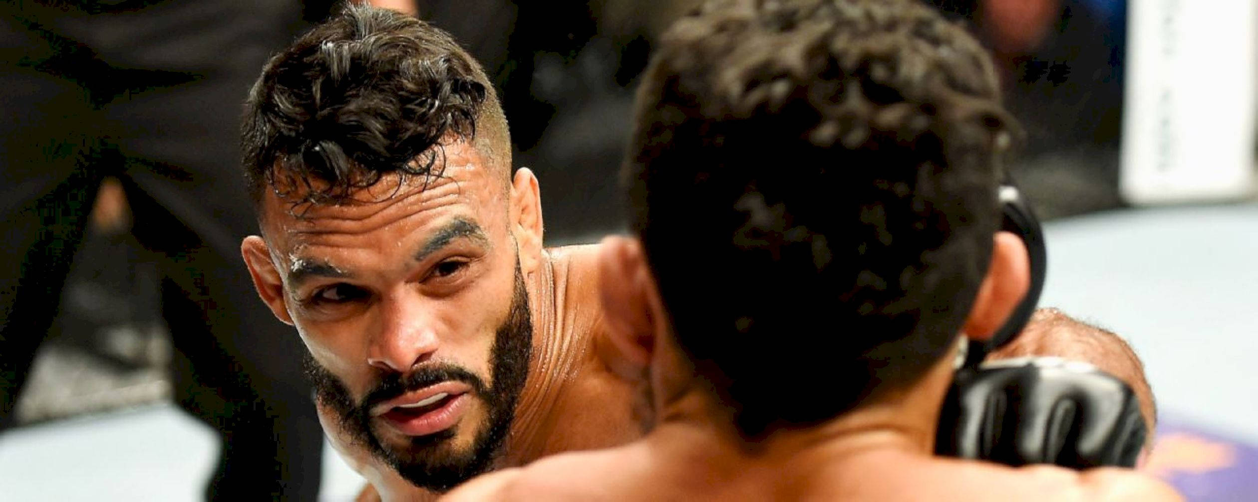 UFC 桌布 壁紙 — 兩名拳手在明亮的競技場燈光下激烈近身纏鬥，汗水在他們肌肉發達的身體上閃閃發光。