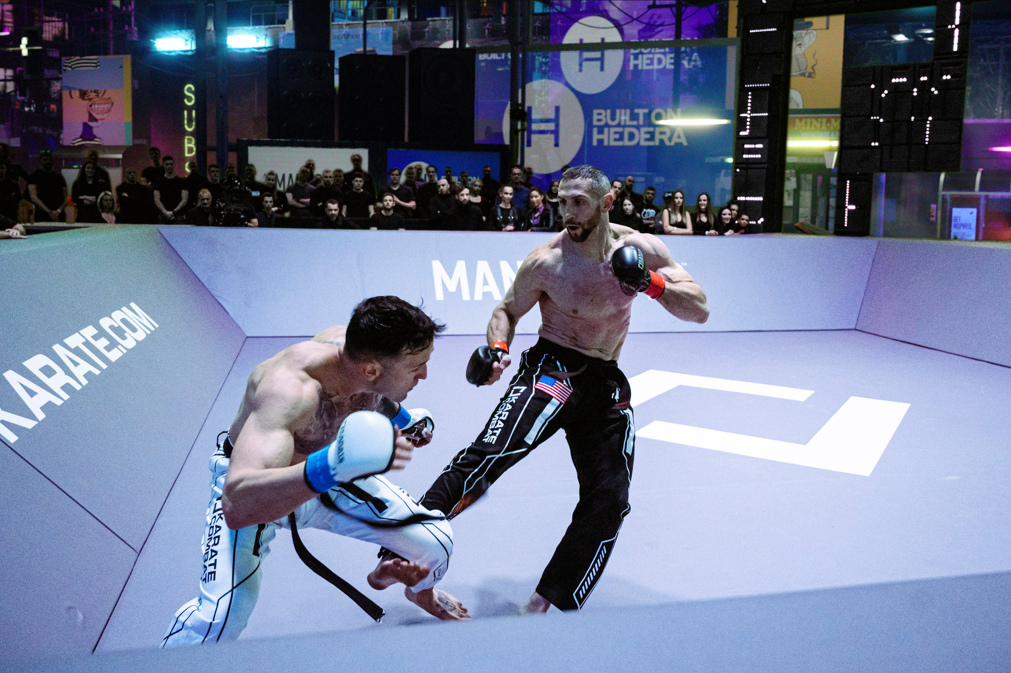 Athletic 桌布 壁紙 — 兩名拳手在燈光明亮的MMA擂台上交鋒，觀眾從看台上觀看。