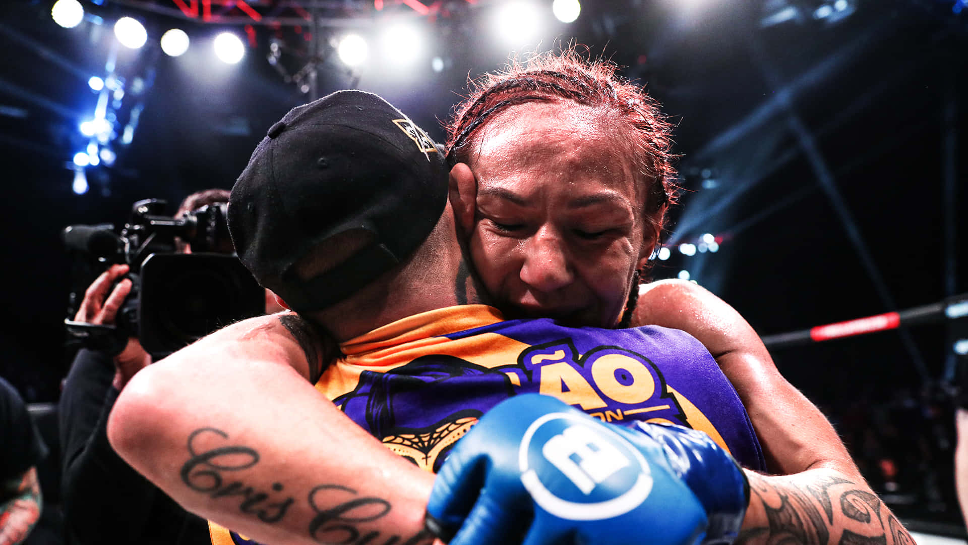 UFC 桌布 壁紙 — 兩名拳手在燈光明亮的競技場上比賽後情感擁抱，周圍閃光燈不斷閃爍。