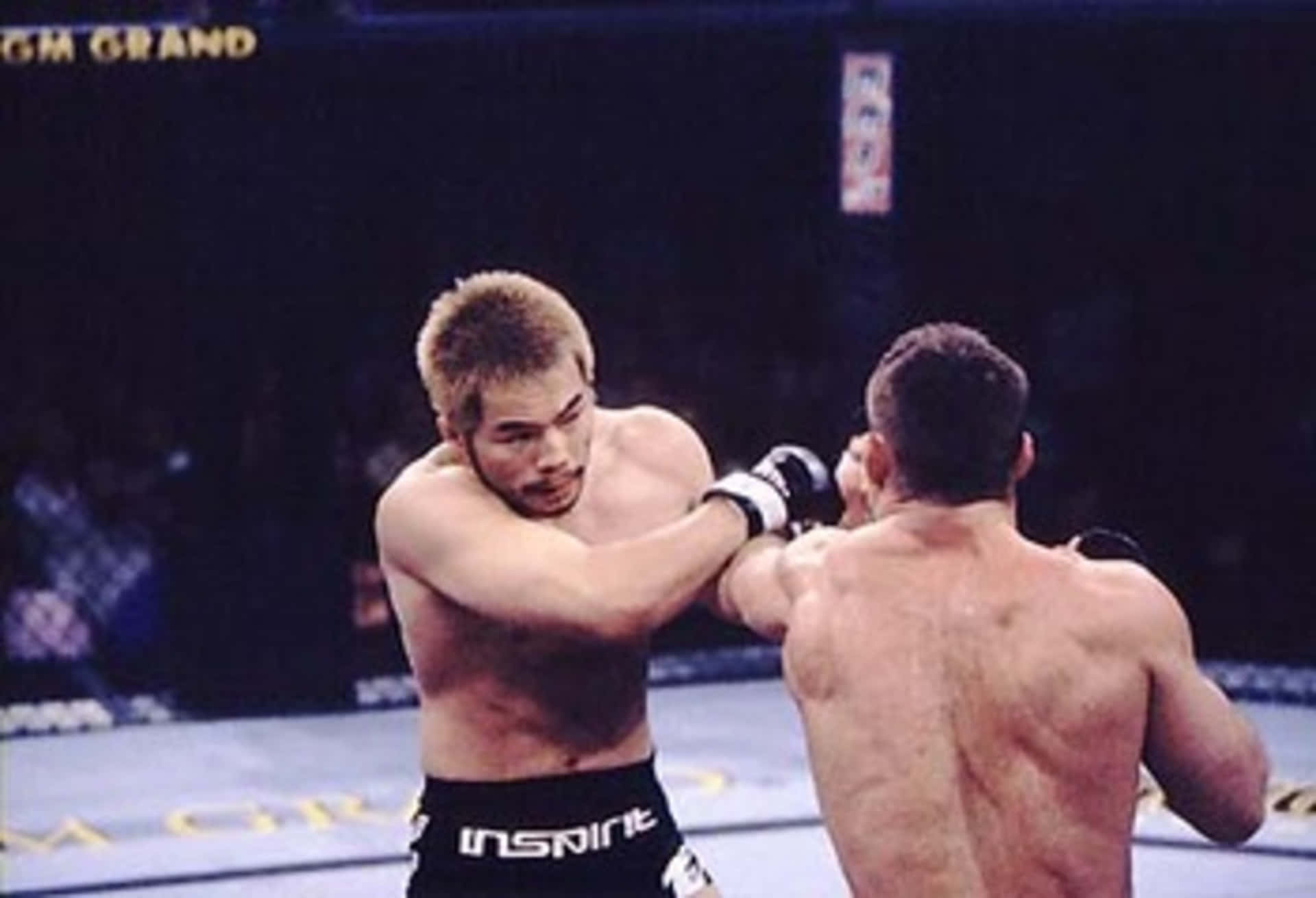 MMA 桌布 壁紙 — 兩名拳手在燈光昏暗的MMA擂台上交鋒，其中一人向對手面部打出強力一拳。