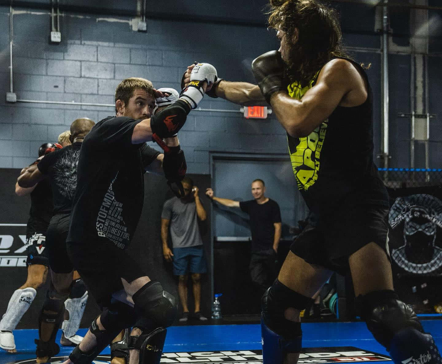 MMA 桌布 壁紙 — 兩名拳手在簡陋的健身房中激烈對戰，汗水飛濺，在明亮的燈光下訓練。