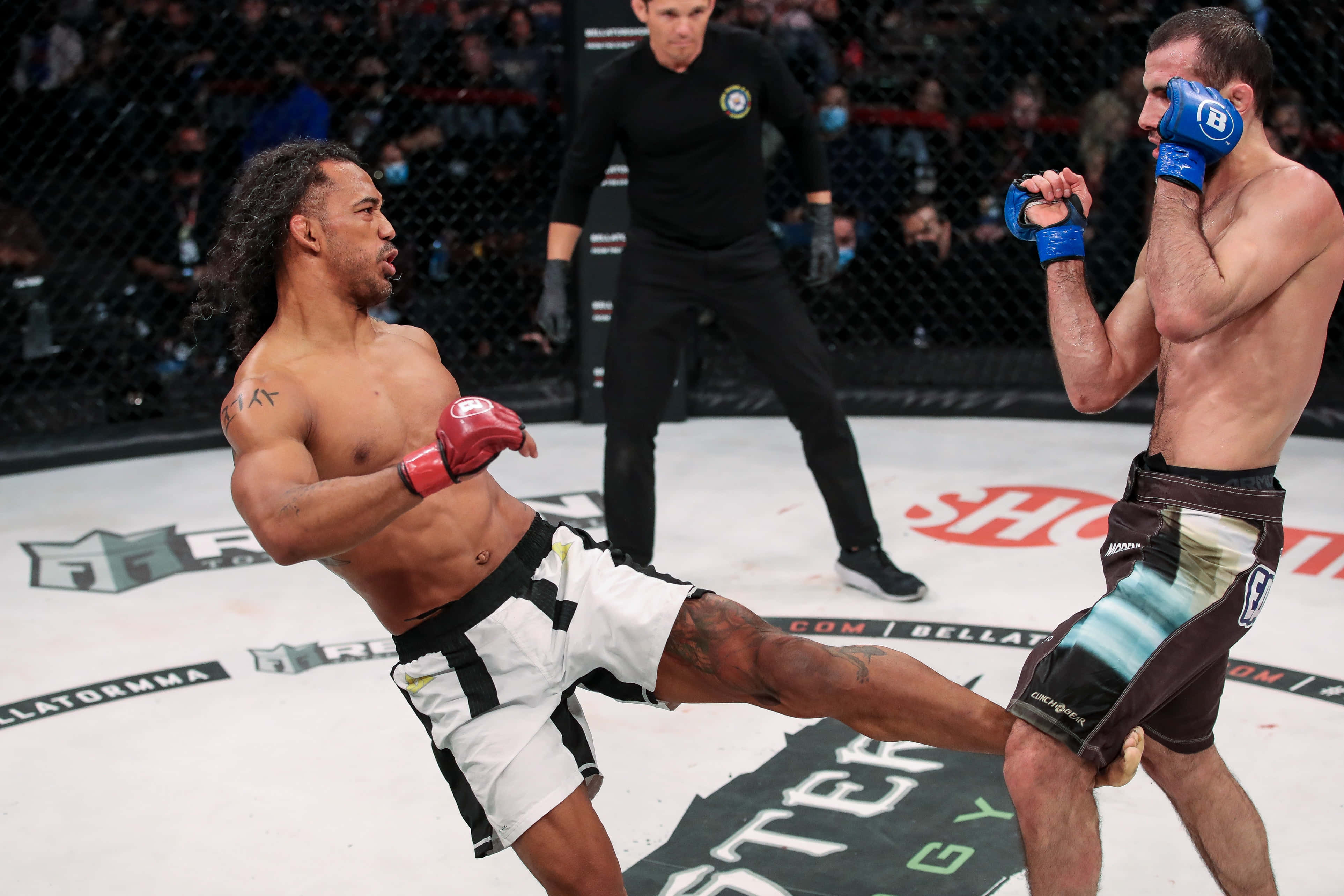 Fight 桌布 壁紙 — 兩名拳手在籠中交鋒，其中一人踢出高踢，裁判專注觀看。