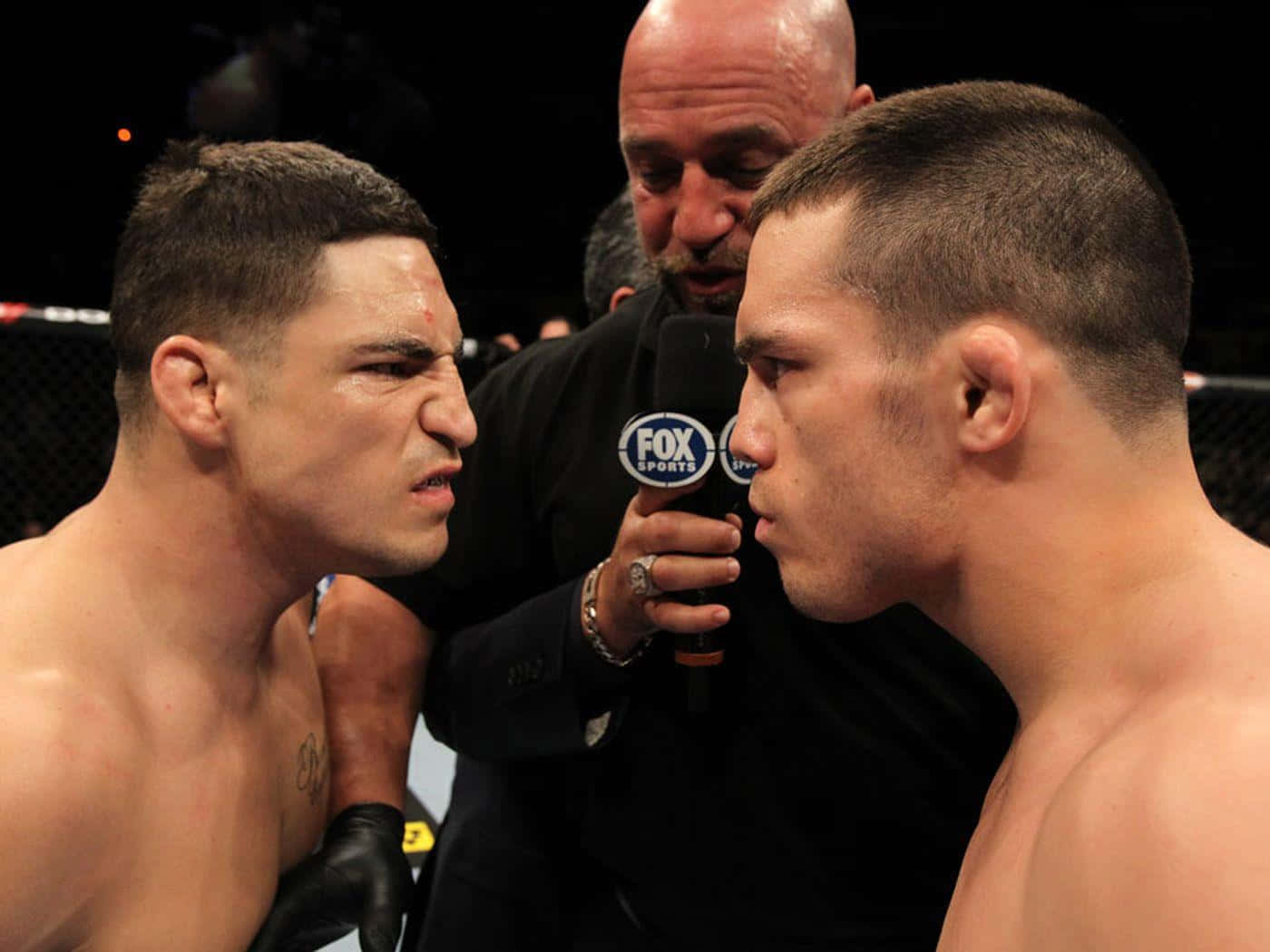 MMA 桌布 壁紙 — 兩名拳手在籠中激烈對視，裁判在他們之間舉著麥克風。