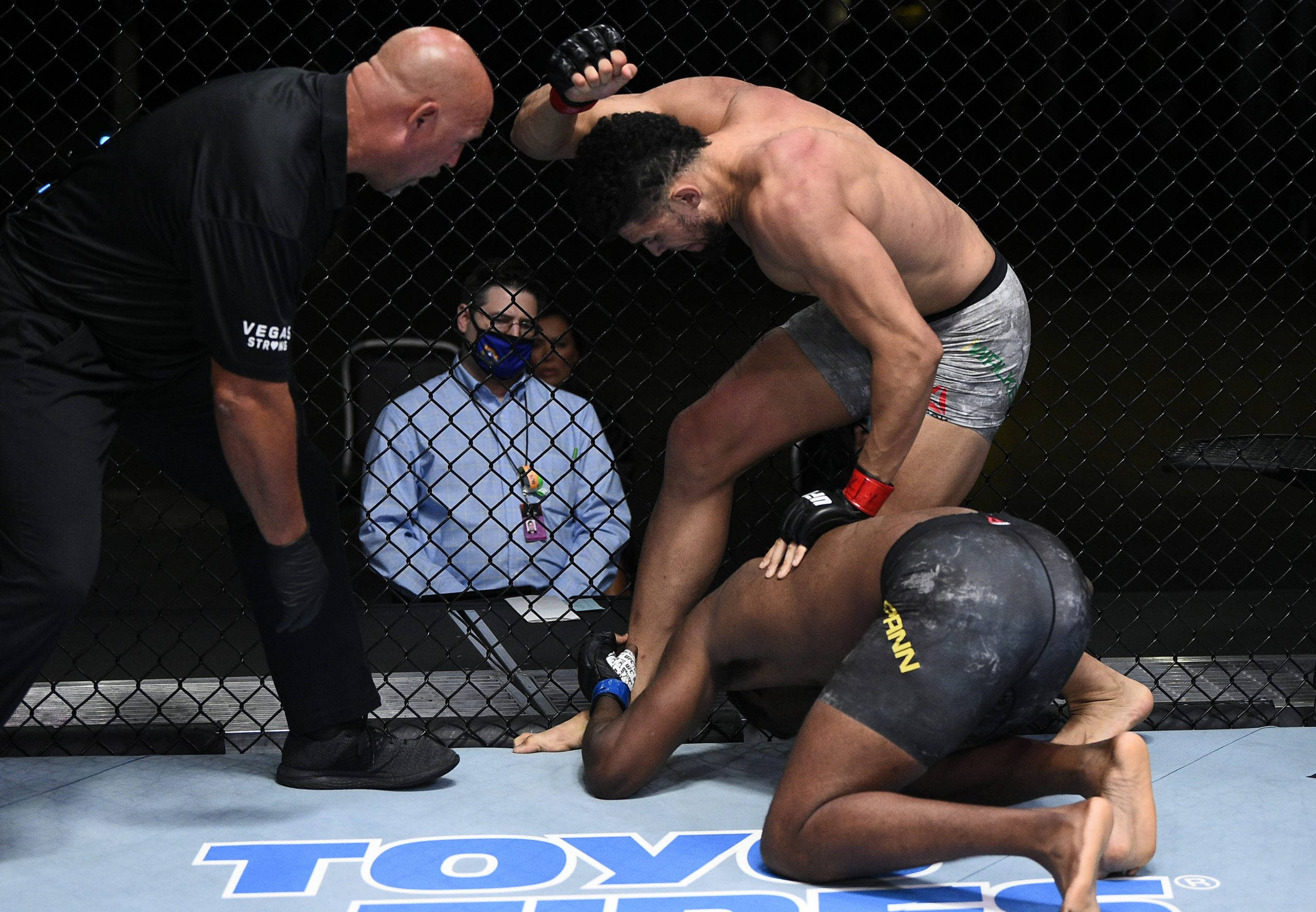 MMA 桌布 壁紙 — 兩名拳手在籠式八角籠內激烈纏鬥，裁判密切監視著比賽進程。