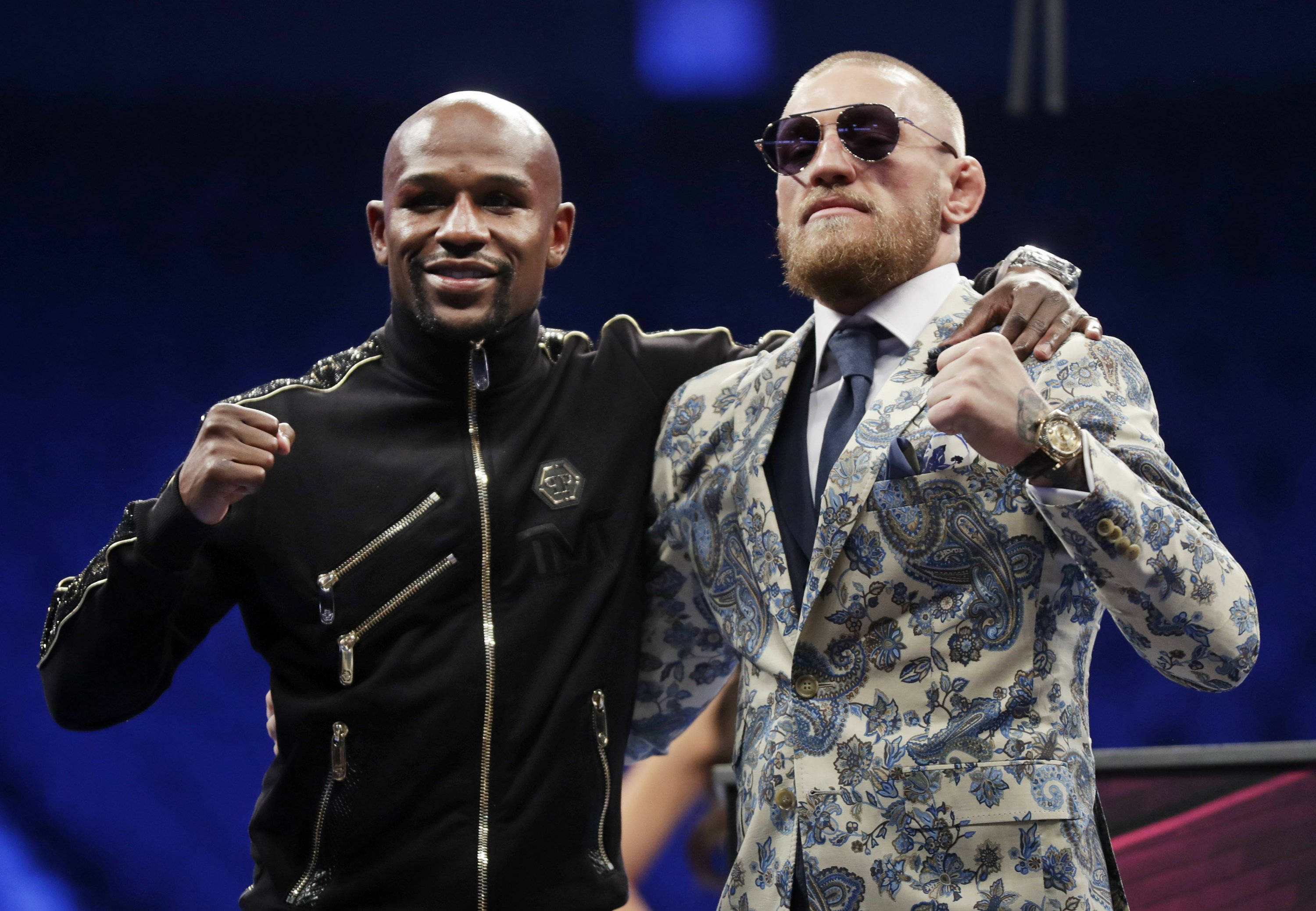 Mcgregor 桌布 壁紙 — 兩名拳手在舞台上自信地擺姿勢，一人穿著黑色拉鍊外套，另一人穿著藍色佩斯利西裝戴太陽眼鏡。