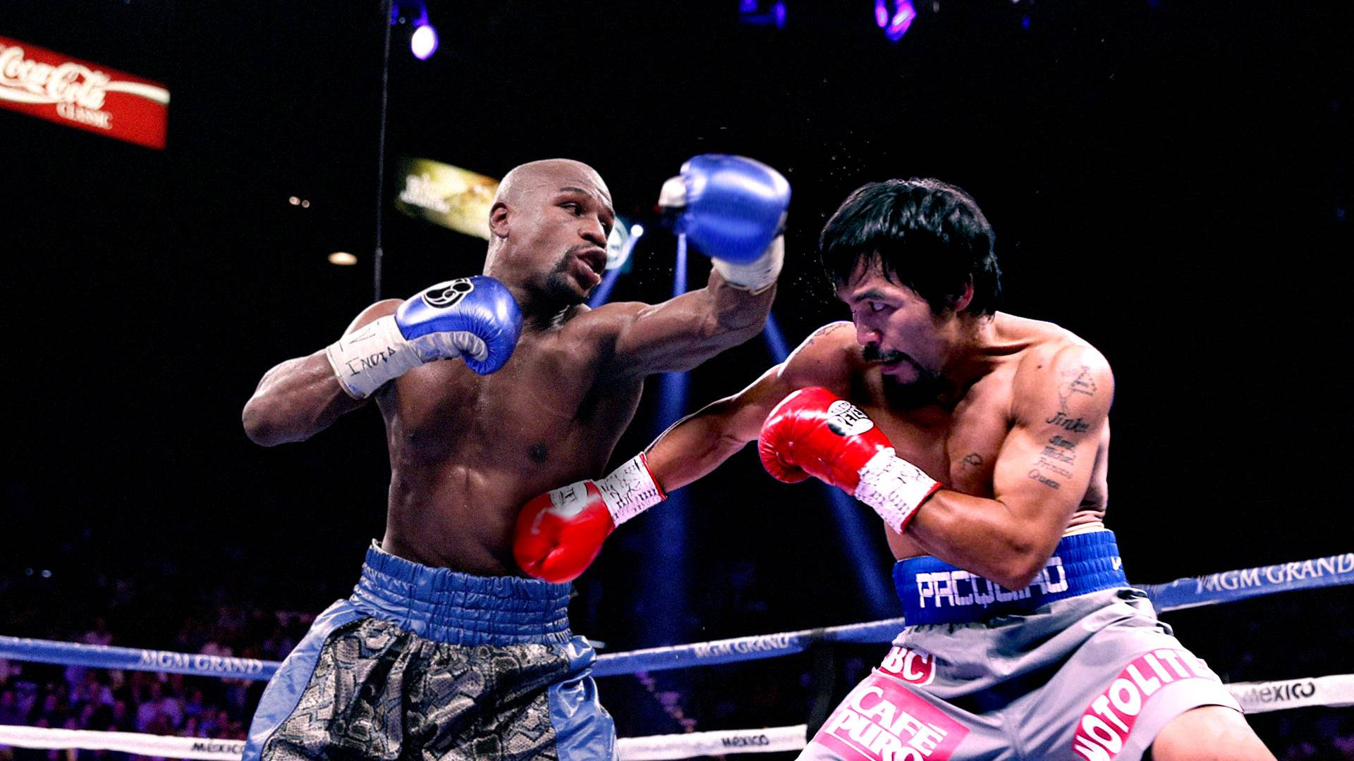Boxing 桌布 壁紙 — 兩名拳擊手在戲劇性的擂台上交鋒，藍色和紅色的手套飛舞，背後觀眾的燈光閃爍。