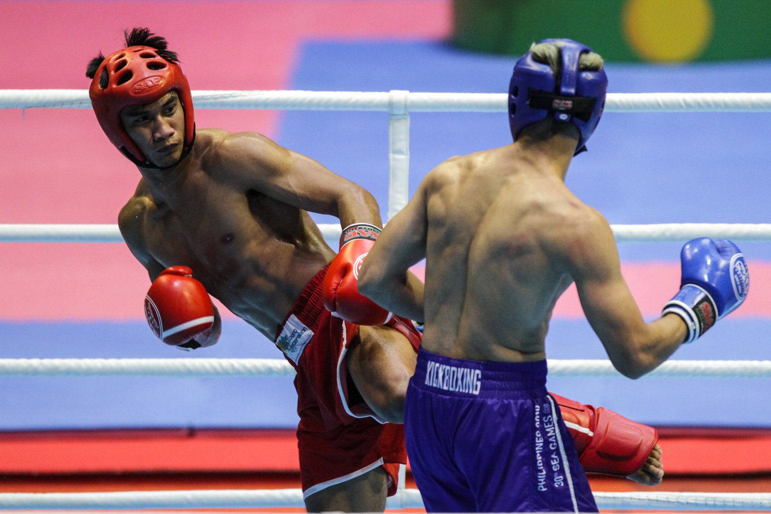 Boxing 桌布 壁紙 — 兩名拳擊手在擂台上交鋒，一名身穿紅色裝備向前猛衝，另一名身穿藍色裝備則以高度專注防守。