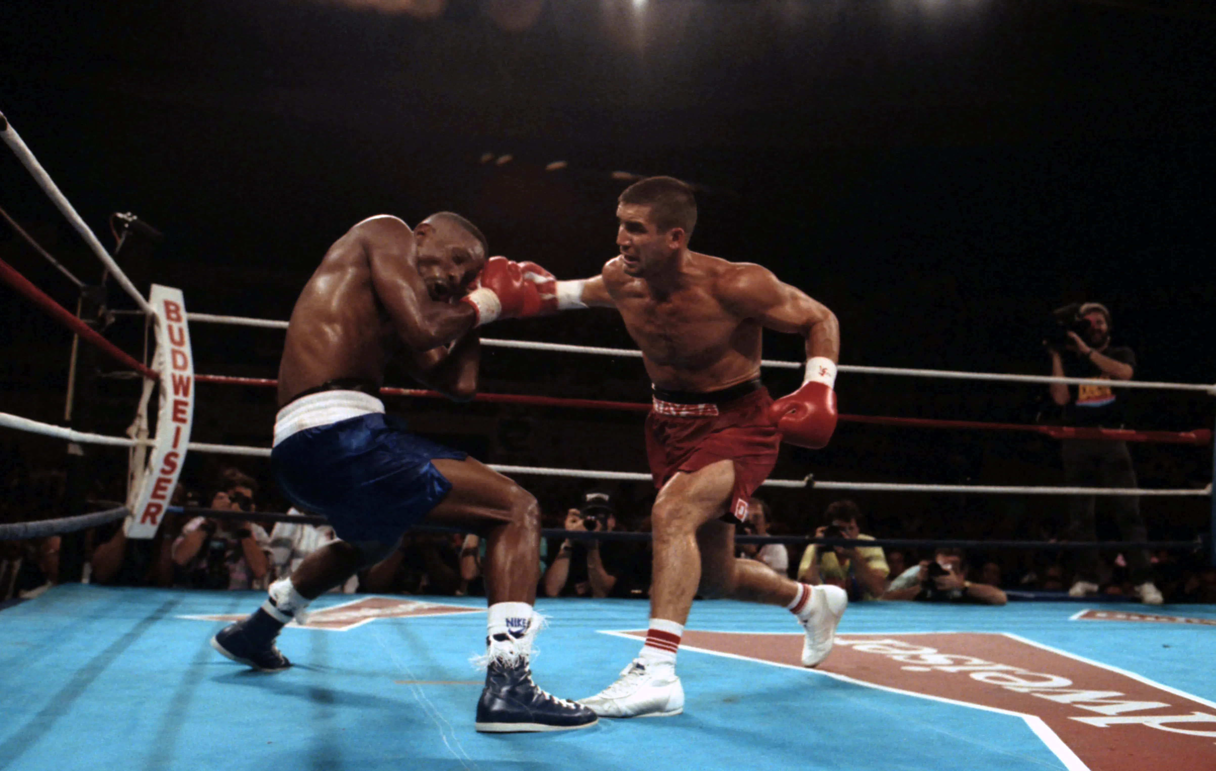 Boxing 桌布 壁紙 — 兩名拳擊手在明亮的場館燈光下，於緊張的擂台時刻交鋒，背景有觀眾和攝影師。