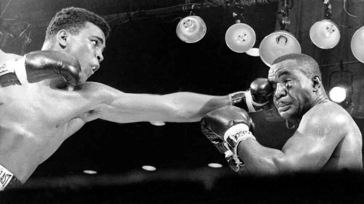 Boxing 桌布 壁紙 — 兩名拳擊手在明亮的頭頂燈光下，於戲劇性的黑白拳擊場場景中交鋒。