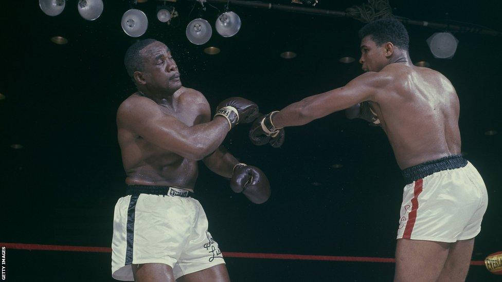 Boxing 桌布 壁紙 — 兩名拳擊手在明亮的頭頂燈光下，於被雨淋濕的擂台上交鋒，一人出拳，另一人阻擋。