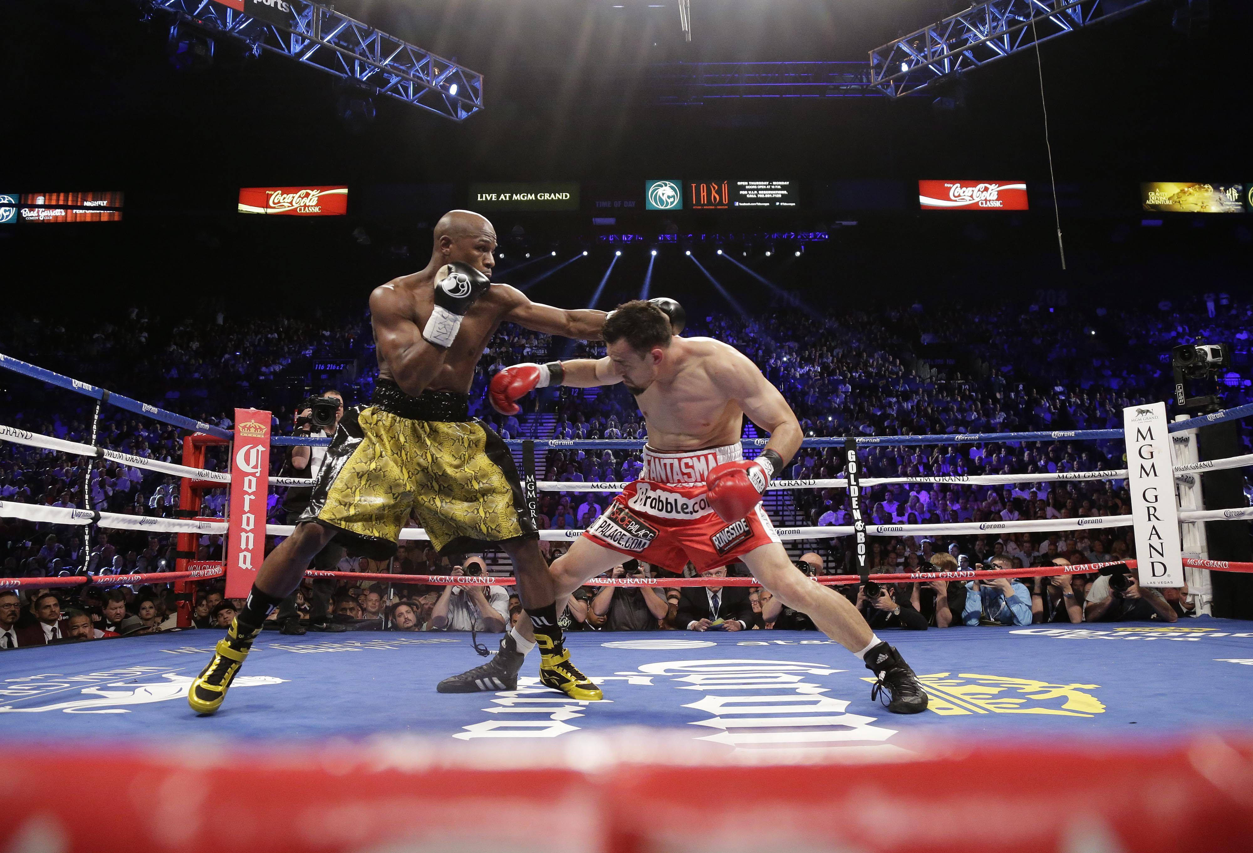 Boxing 桌布 壁紙 — 兩名拳擊手在燈光明亮的擂台上交鋒，觀眾在場館燈光下專注觀看。