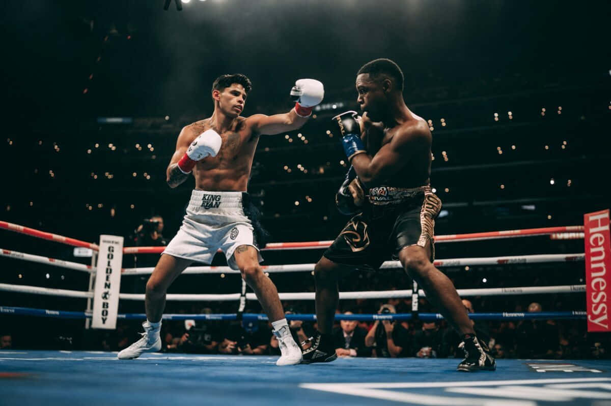 Ryan Garcia 桌布 壁紙 — 兩名拳擊手在燈光明亮的擂台上交鋒，一人出拳，另一人在場館燈光下防守。