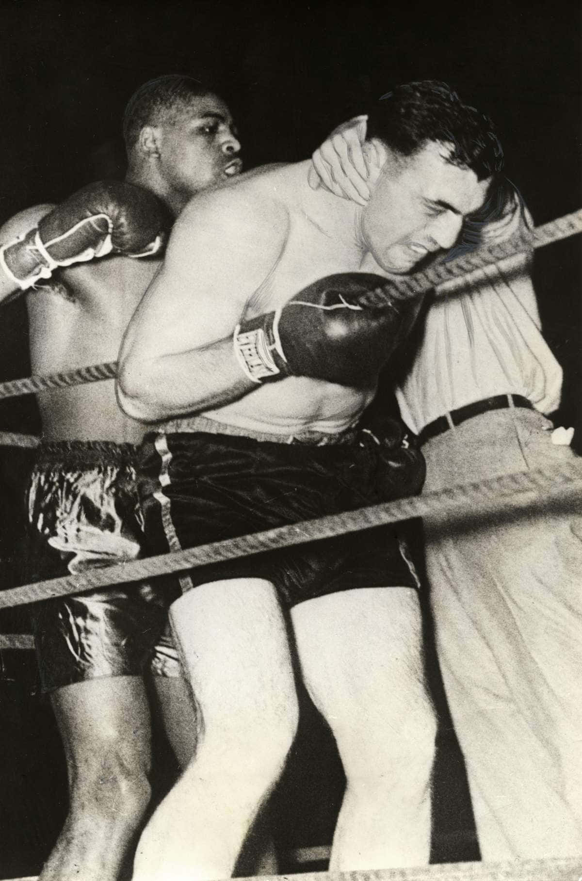 Boxing 桌布 壁紙 — 兩名拳擊手在燈光昏暗的擂台上激烈纏鬥，繩索和裁判在附近。