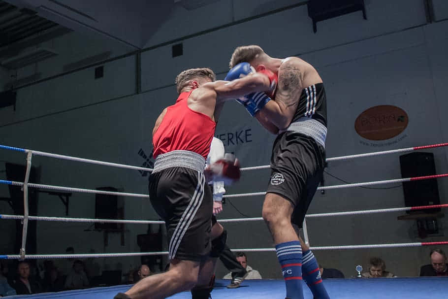 運動 桌布 壁紙 — 兩名拳擊手在緊張的擂台上交鋒，紅衣者揮出一拳，黑衣者則舉起手套防守。