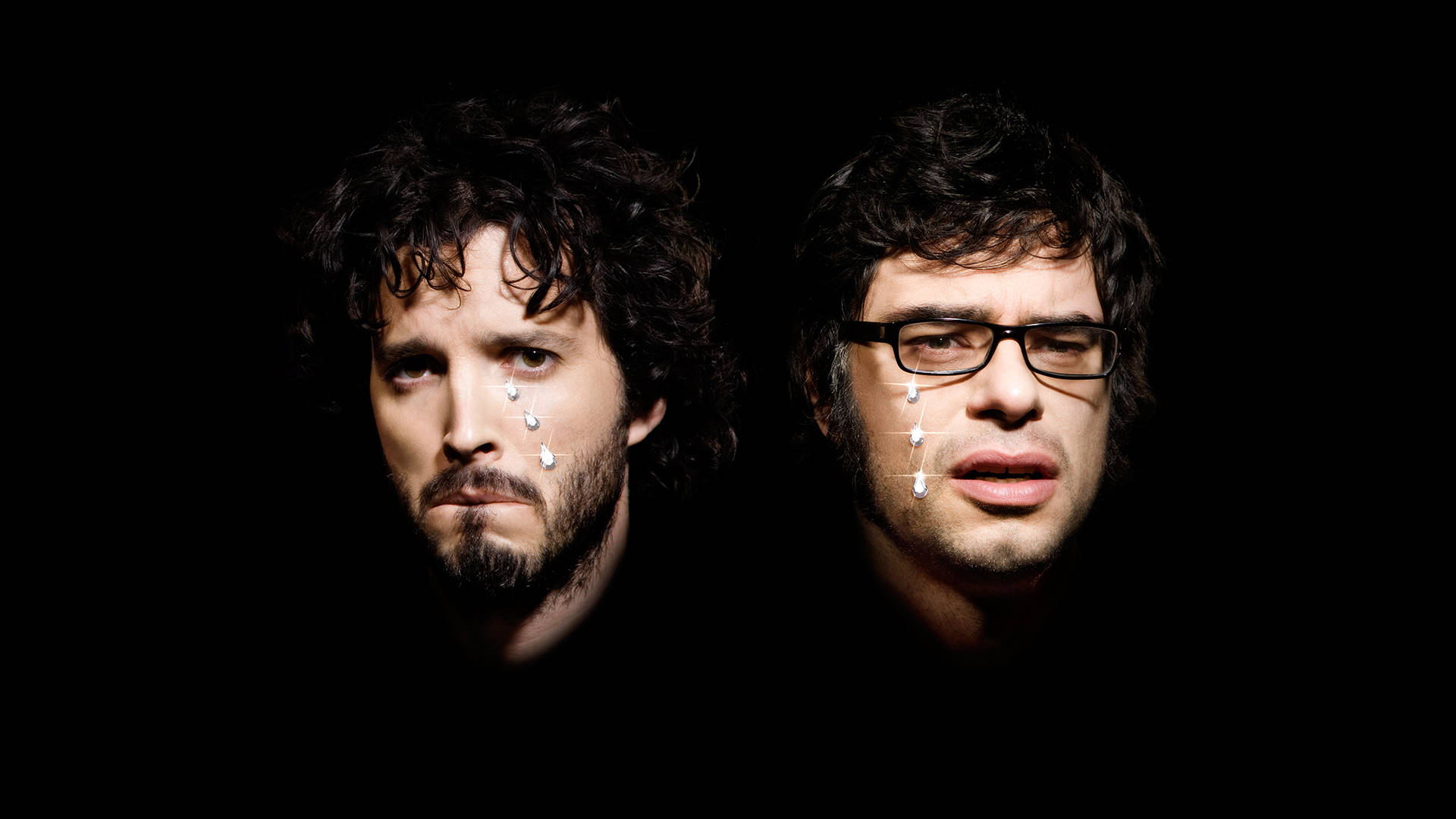 Flight Of The Conchords 桌布 壁紙 — 兩名捲髮戴眼鏡的男子在黑色背景前，臉上帶有白色水滴效果，凝視著鏡頭。
