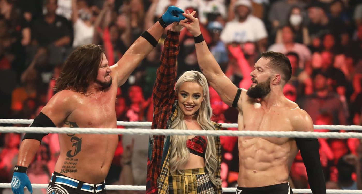 WWE 桌布 壁紙 — 兩名摔角手和一名穿著格紋衫的金髮女子在擂台上慶祝勝利，身後有歡呼的粉絲。