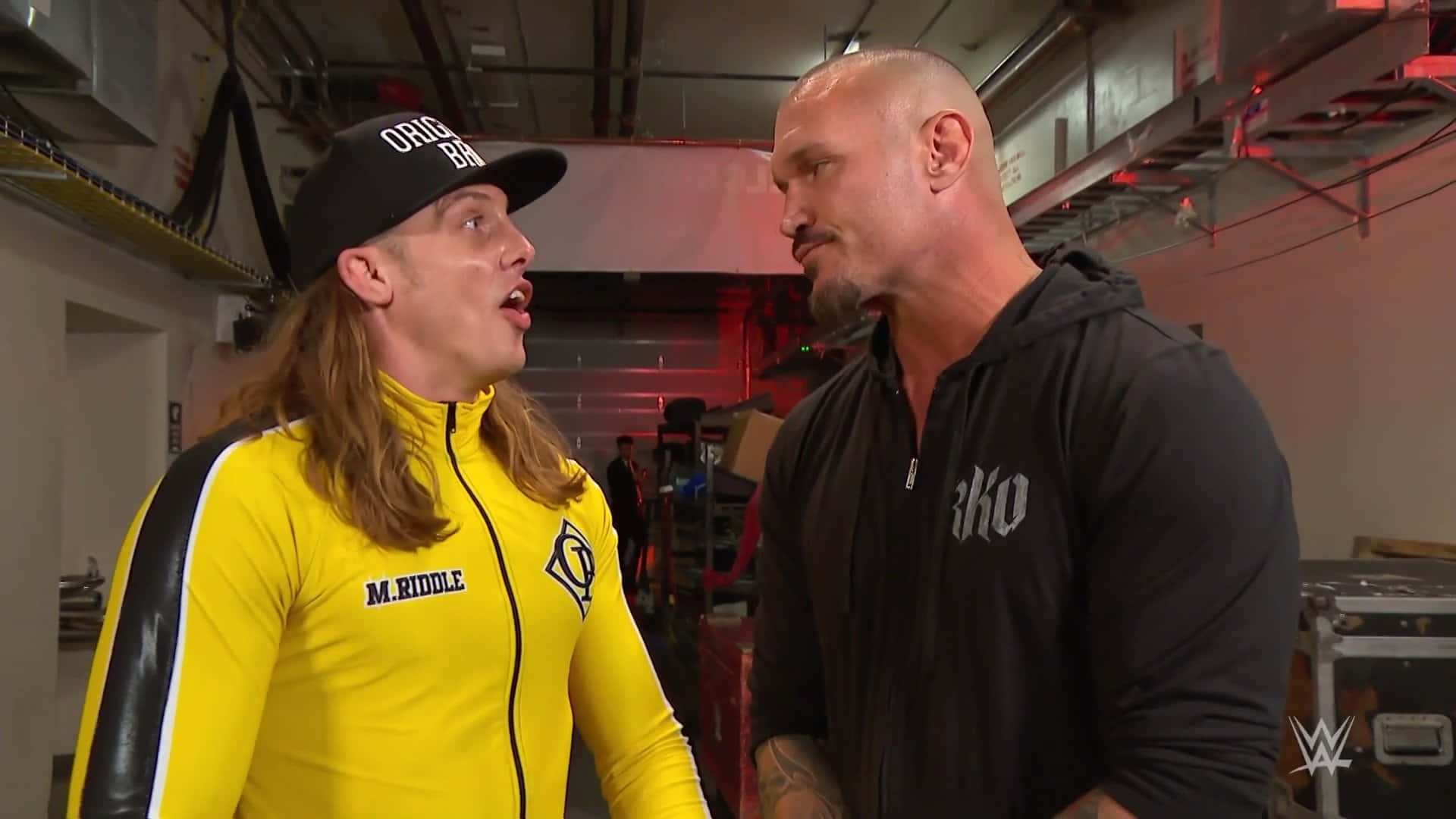 randy orton 桌布 壁紙 — 兩名摔角手在後台區域對峙，一人身穿亮黃色西裝，另一人穿著黑色連帽衫。