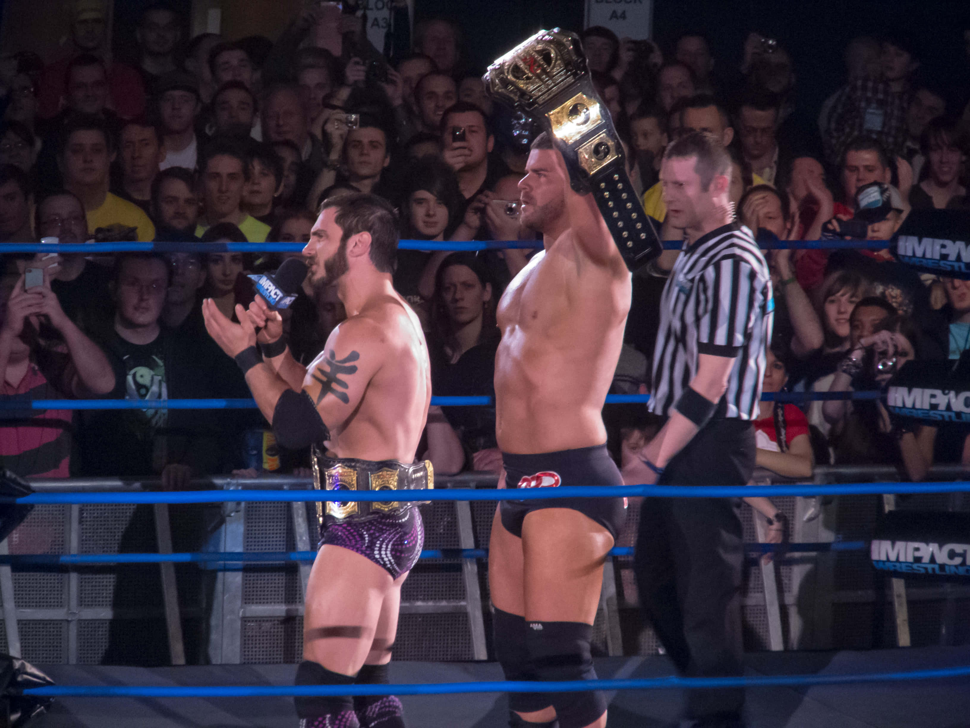WWE 桌布 壁紙 — 兩名摔角手在擂台上，一人手持冠軍腰帶，另一人在明亮的場館燈光下對著麥克風說話。