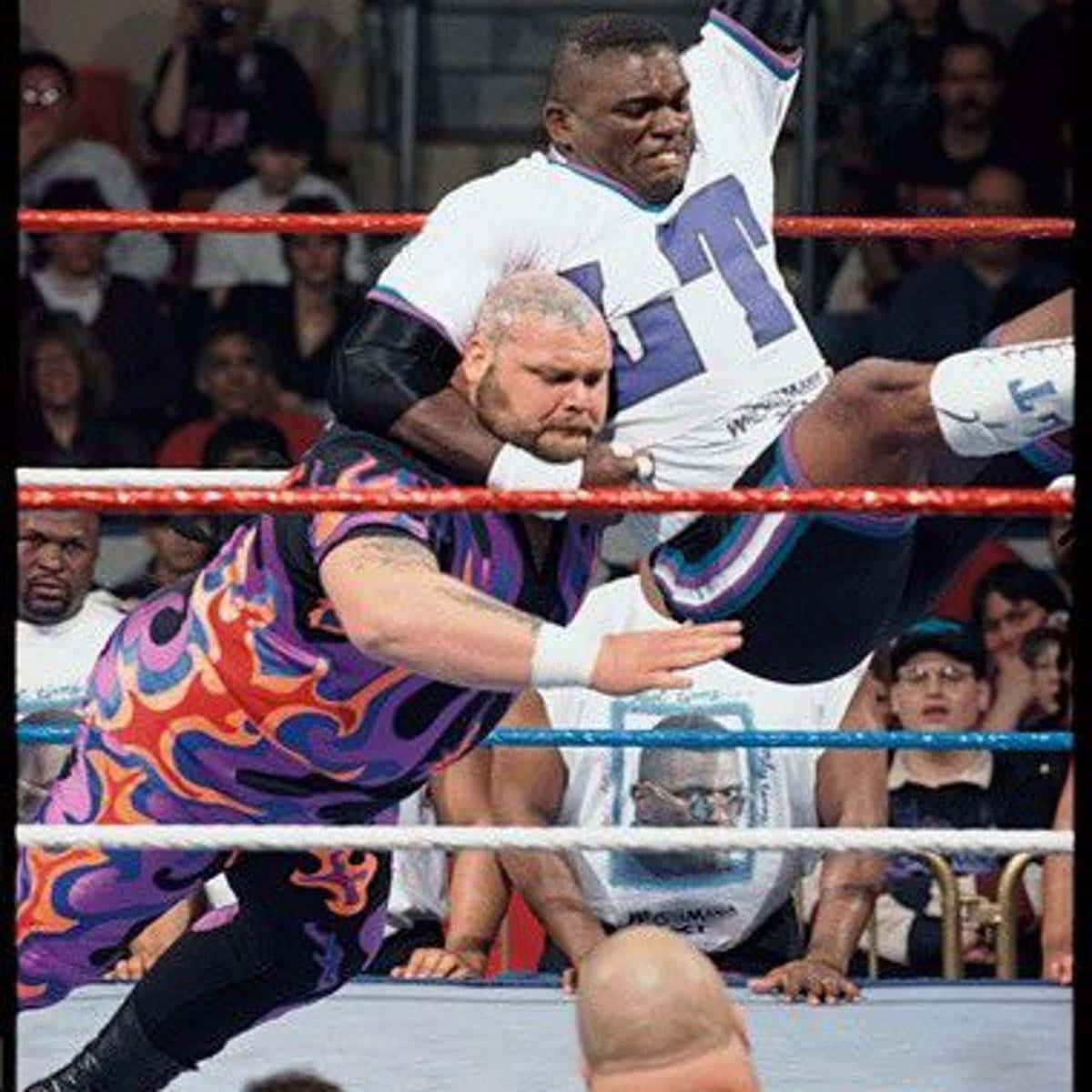 WWE 桌布 壁紙 — 兩名摔角手在擂台上交鋒，一人將另一人舉起，在觀眾的歡呼聲中施展高衝擊力招式。