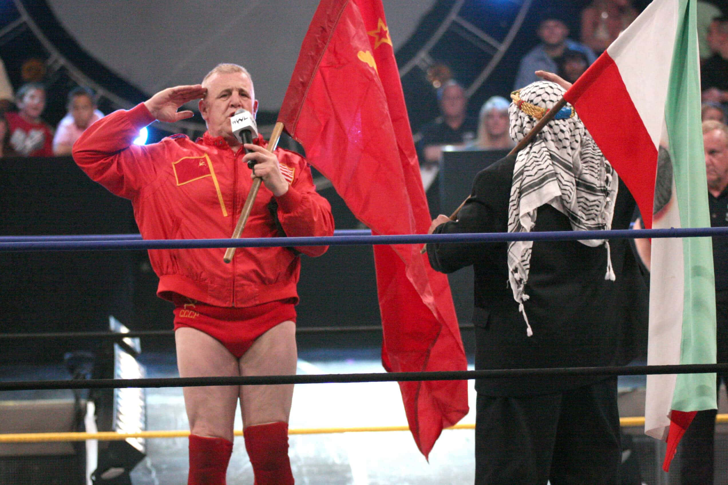 WWE 桌布 壁紙 — 兩名摔角手在擂台上向中國和巴勒斯坦國旗敬禮，場館燈光下。