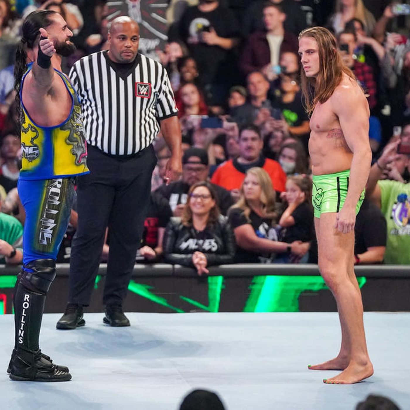 seth rollins 桌布 壁紙 — 兩名摔角手在擂台上對峙，中間有裁判，觀眾專注觀看。