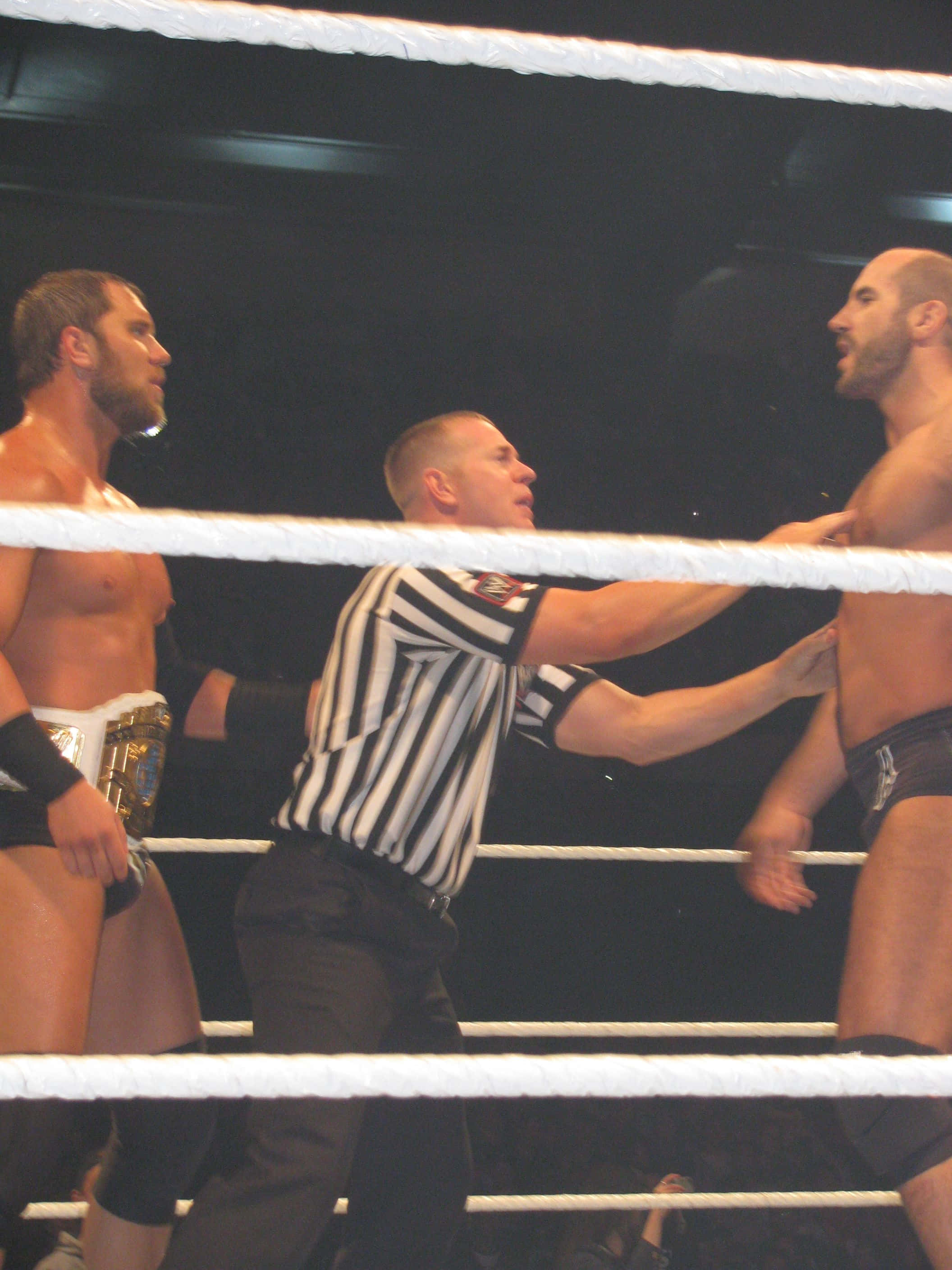 WWE 桌布 壁紙 — 兩名摔角手在擂台上對峙，裁判在明亮的場館燈光下將他們分開。