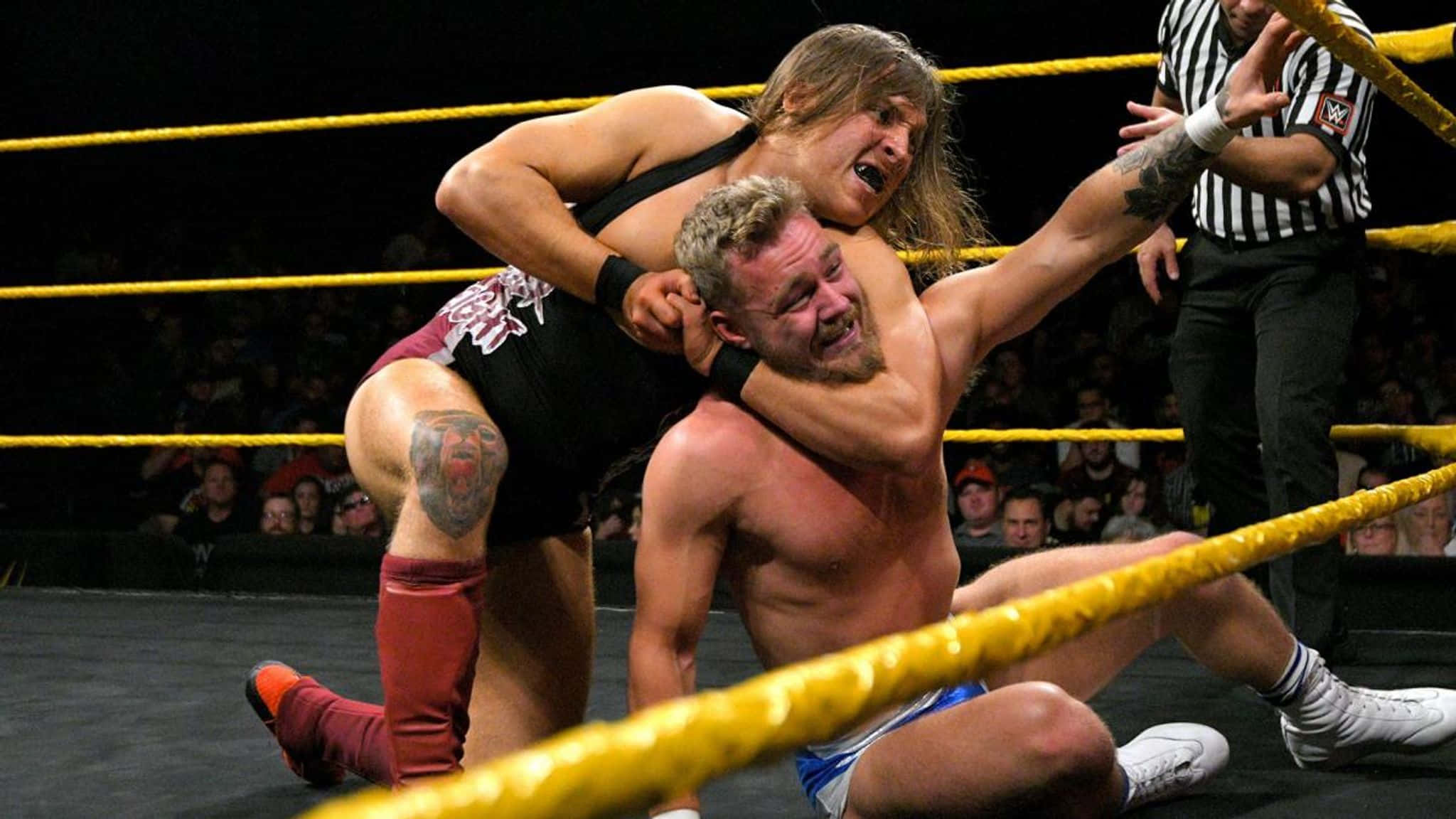 WWE 桌布 壁紙 — 兩名摔角手在擂台上激烈糾纏，裁判在旁觀看，觀眾在背景中歡呼。