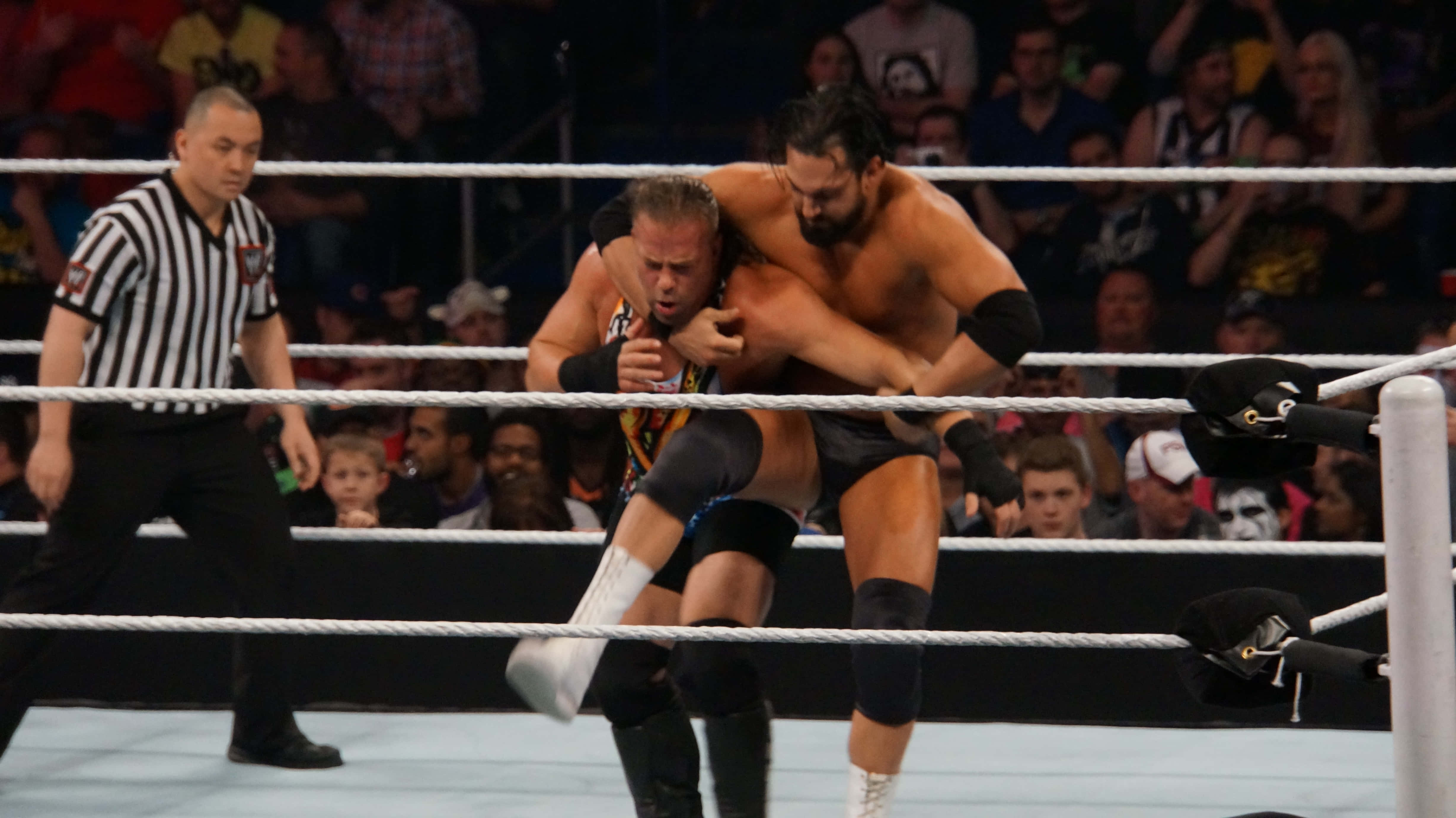 WWE 桌布 壁紙 — 兩名摔角手在擂台上激烈糾纏，裁判在旁觀看，觀眾在看台上歡呼。